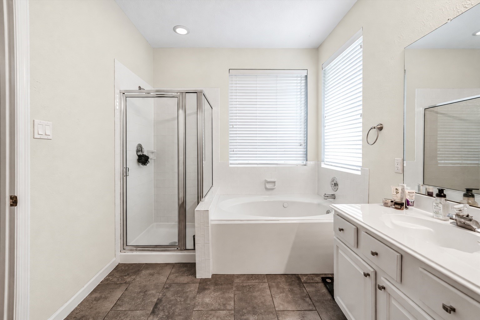 Spacious main bathroom featuring a luxurious soaking tub, separate glass-enclosed shower, and ample natural light, complemented by a sleek vanity with plenty of storage.