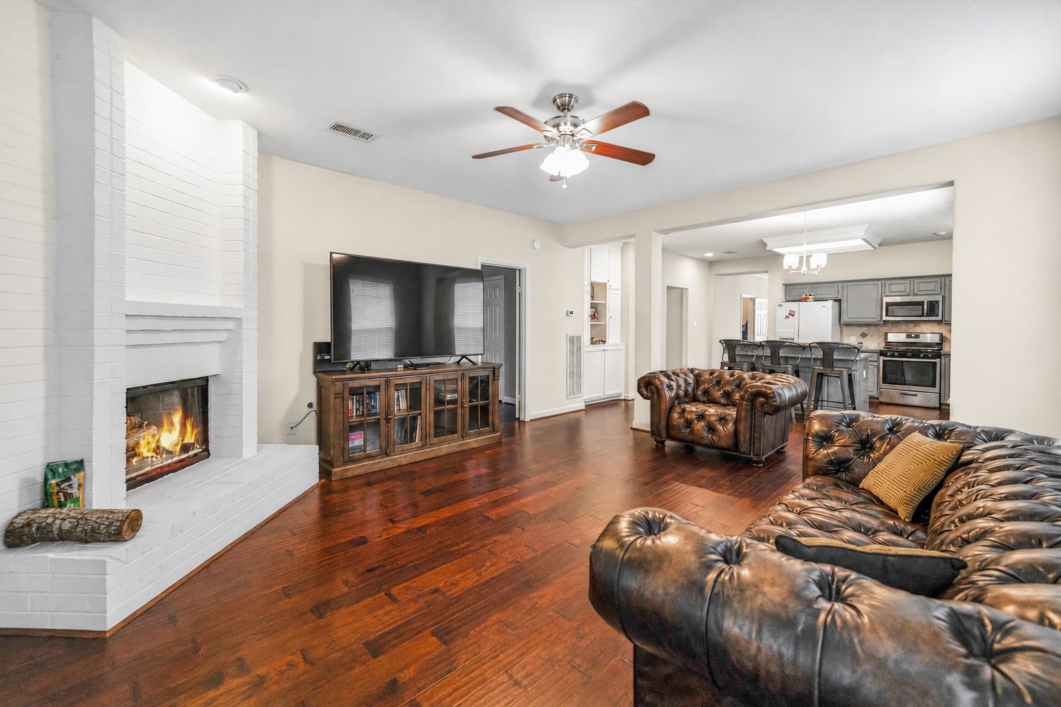 Spacious living area featuring a cozy fireplace, elegant hardwood floors, and an open layout connecting to a modern kitchen with stainless steel appliances.