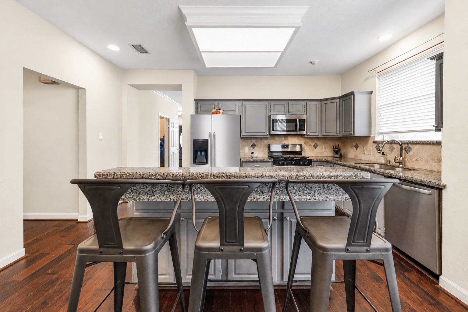 Modern kitchen with sleek granite countertops, stainless steel appliances, and stylish gray cabinetry, complemented by a cozy breakfast bar with seating. Modern kitchen with sleek granite countertops, stainless steel appliances, and stylish gray cabinetry, complemented by a cozy breakfast bar with seating.
