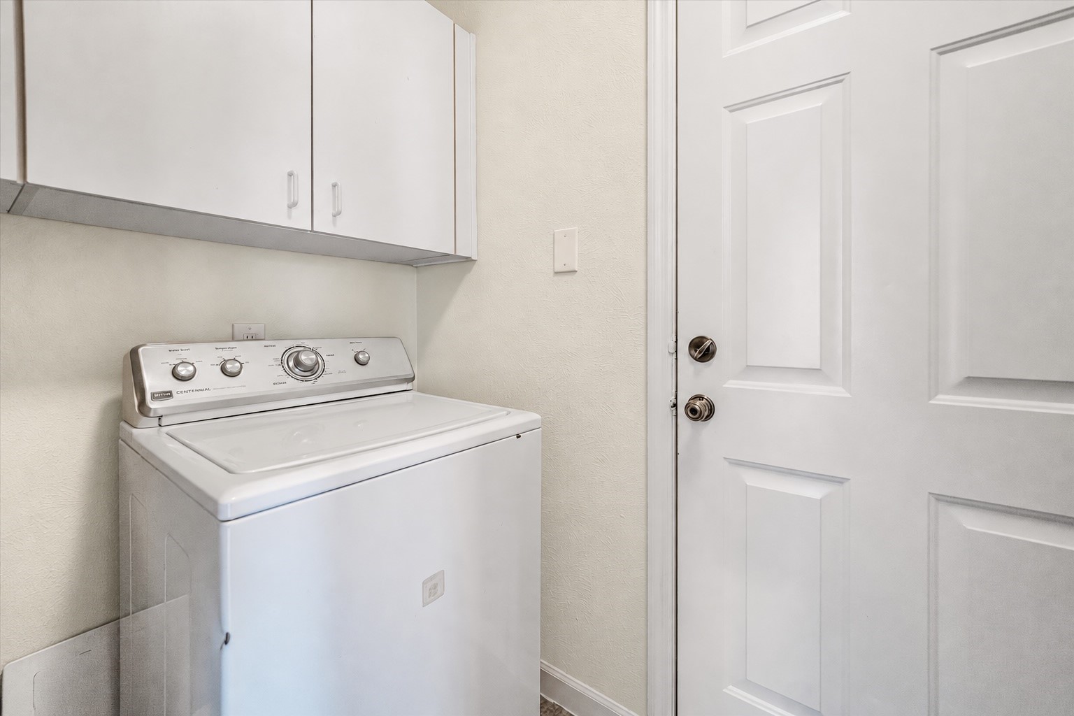 Compact laundry area featuring a top-loading washing machine and overhead storage cabinets, conveniently located next to an exterior door.