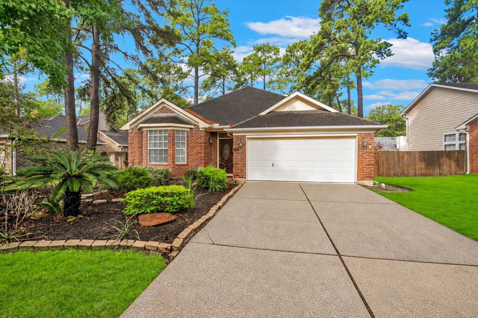 Charming brick home with a welcoming front yard and lush landscaping, featuring a spacious driveway leading to a two-car garage.