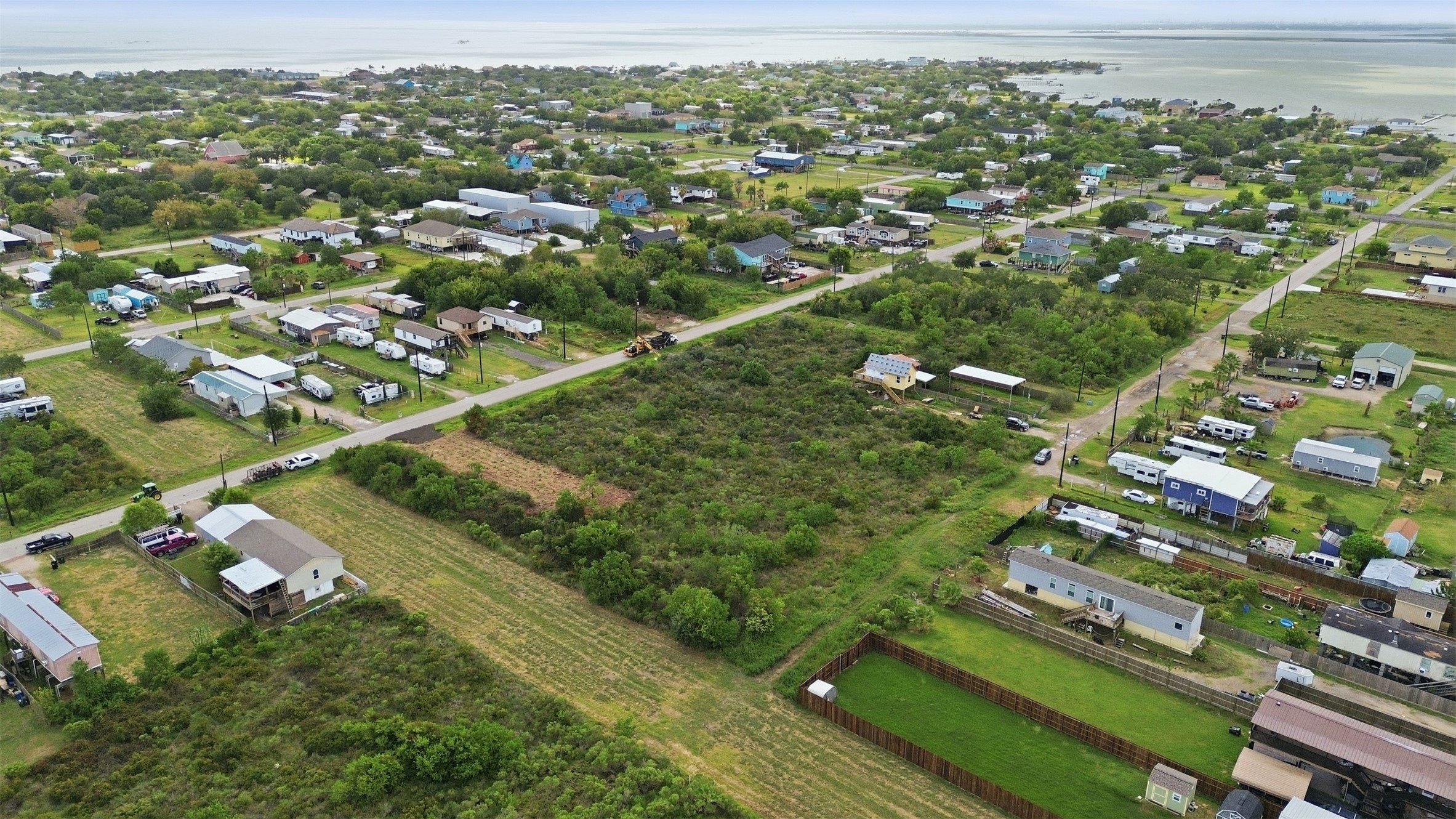 Angled aerial showing the full tract, with the bay on the horizon. Surrounding lots hold a mix of stilted coastal homes and cottages.