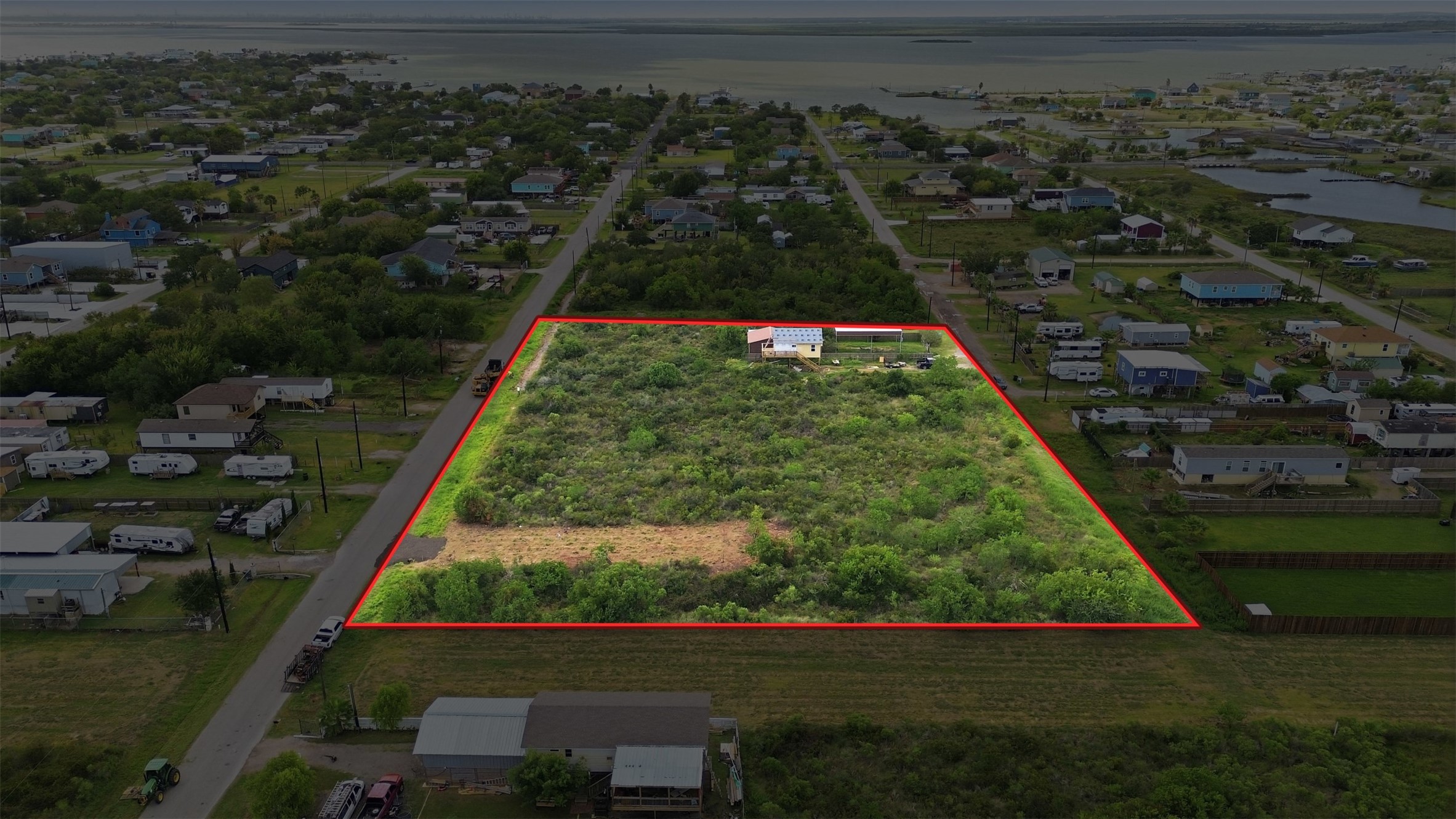 Aerial with a red outline marking the approximate property boundary. The bay and tidal waterways are visible beyond.