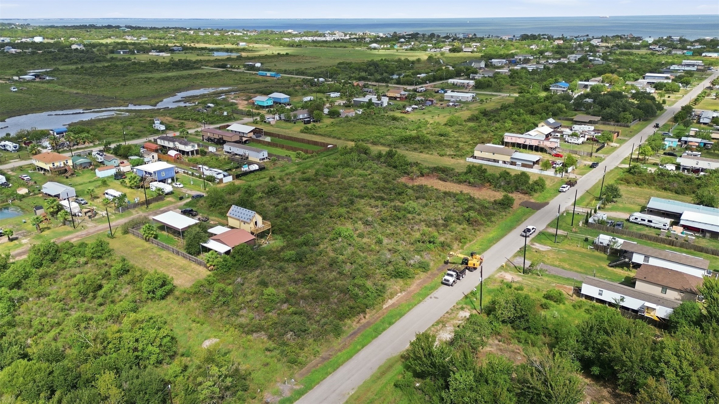 View along the paved street with open marsh and tidal water on one side and the bay on the horizon. Neighboring lots are developed with homes and outbuildings.
