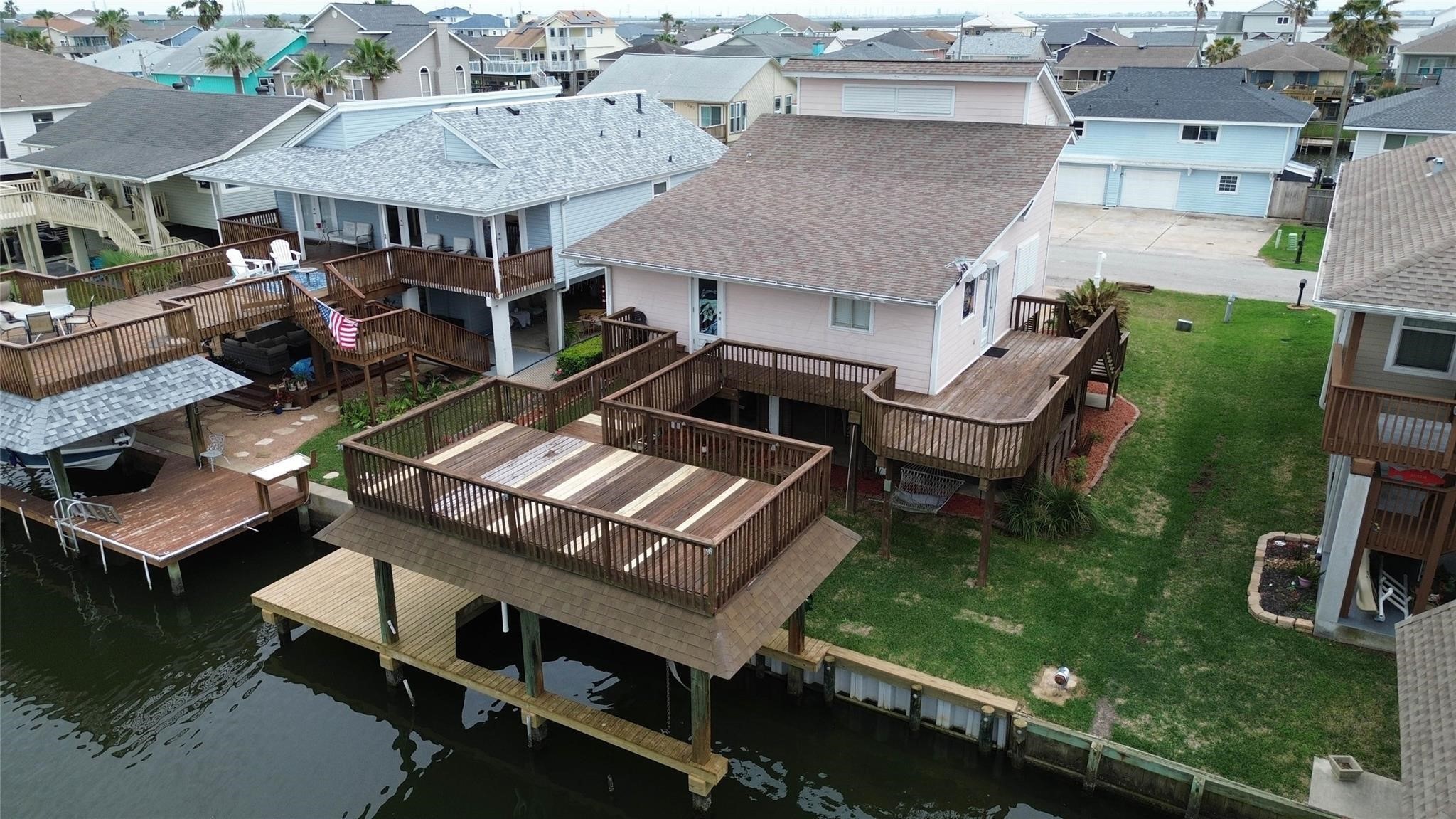 This waterfront home features a spacious deck overlooking a canal, providing direct water access. The house has a large wooden patio and a well-maintained lawn, perfect for outdoor activities and relaxation. The surrounding neighborhood consists of similar homes, creating a pleasant, coastal community atmosphere.