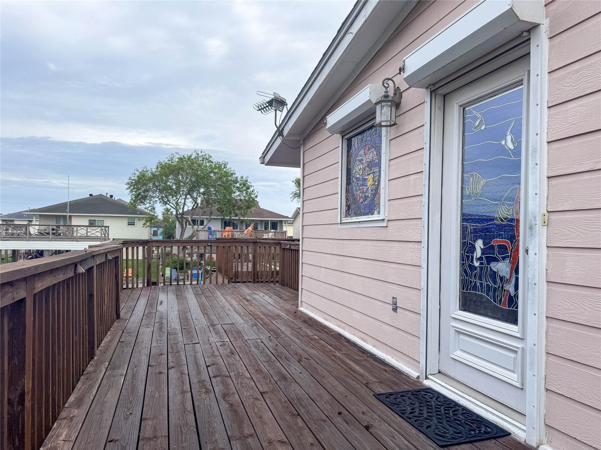 This photo showcases a charming deck with wooden flooring, adjacent to a house with light-colored siding. It features a decorative glass door and window, offering a blend of privacy and artistic flair. The view includes neighboring homes and greenery, indicating a cozy neighborhood setting.