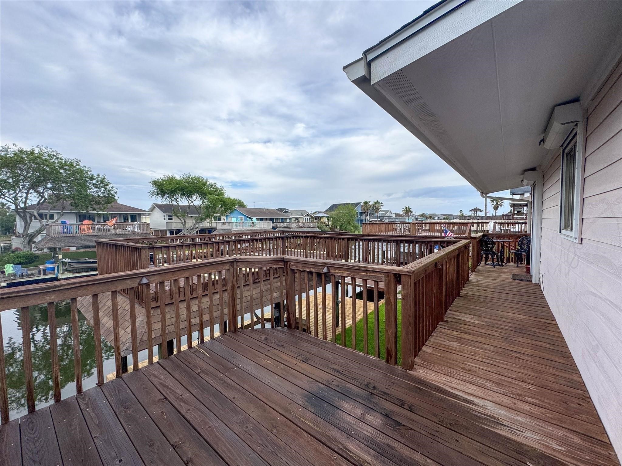 This photo showcases a waterside home with a spacious wooden deck overlooking a canal, ideal for outdoor relaxation. The surrounding neighborhood features similar waterfront properties, providing a serene and picturesque setting.