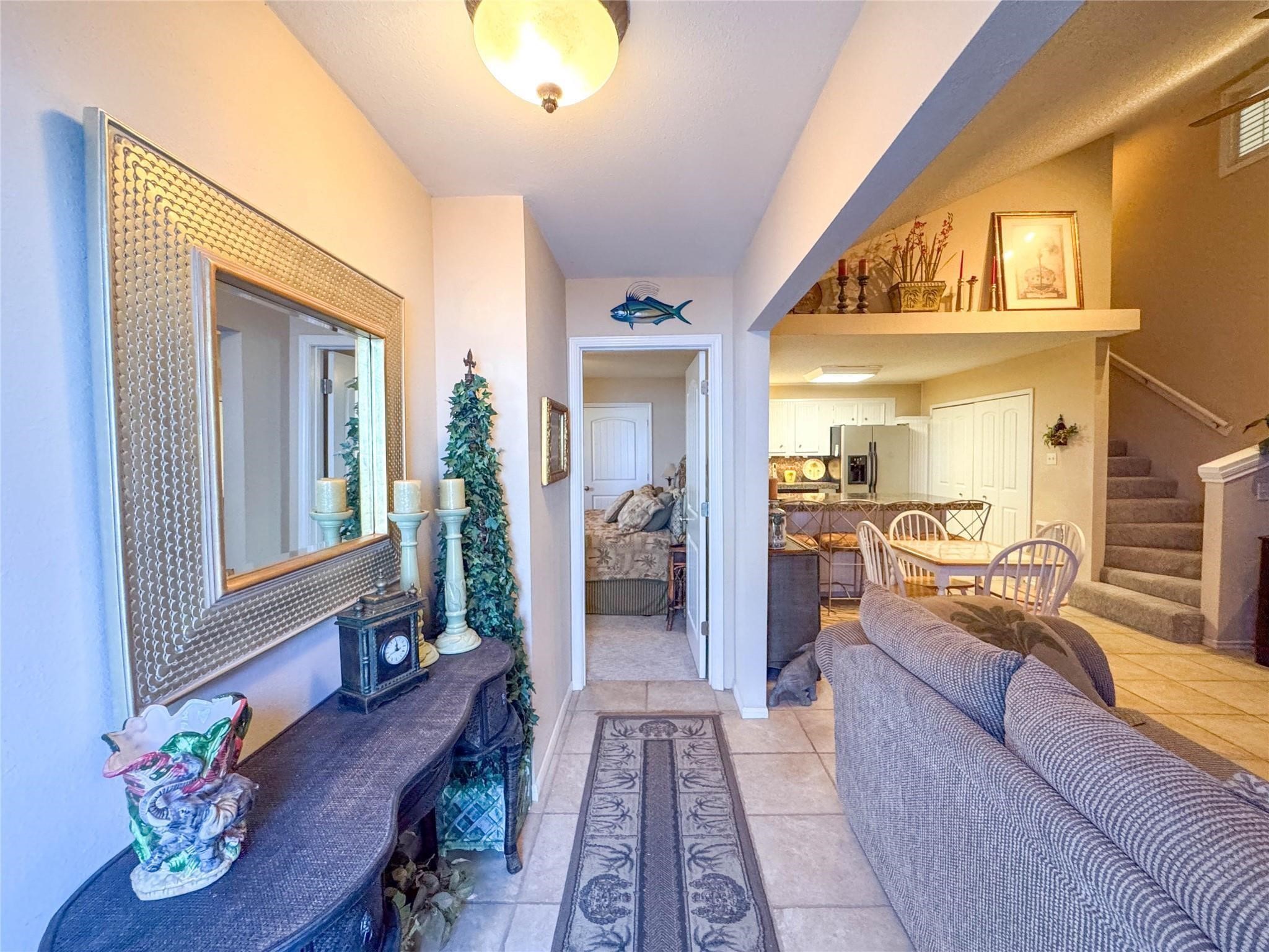 This welcoming entryway features a cozy living space with neutral tones and tile flooring. It opens into a kitchen and dining area with ample natural light. A staircase leads upstairs, providing easy access to additional rooms.