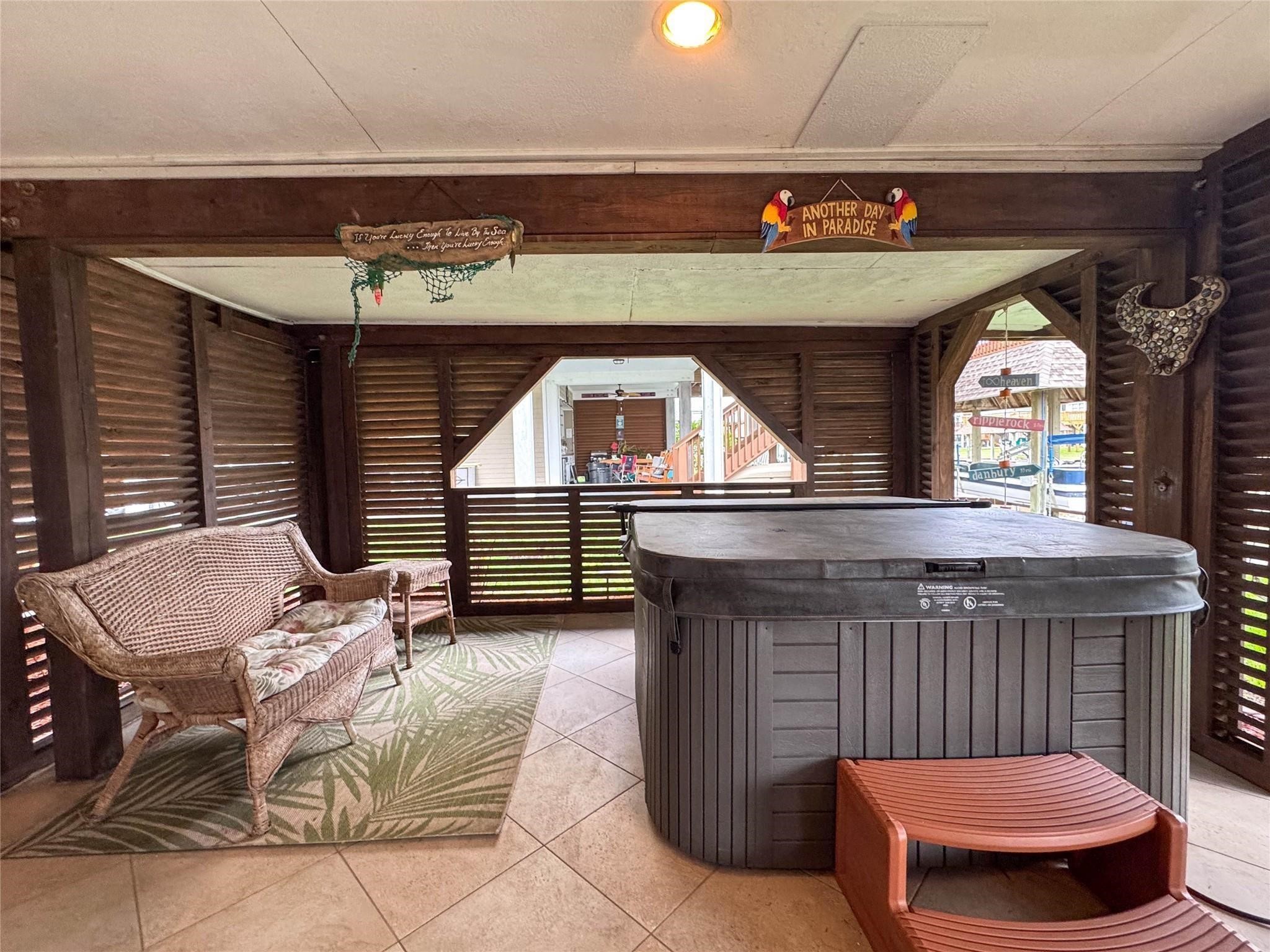 This cozy screened-in porch features a hot tub, wicker seating, and a tropical rug, perfect for relaxation. The wooden accents and decor create a laid-back, paradise-inspired atmosphere.