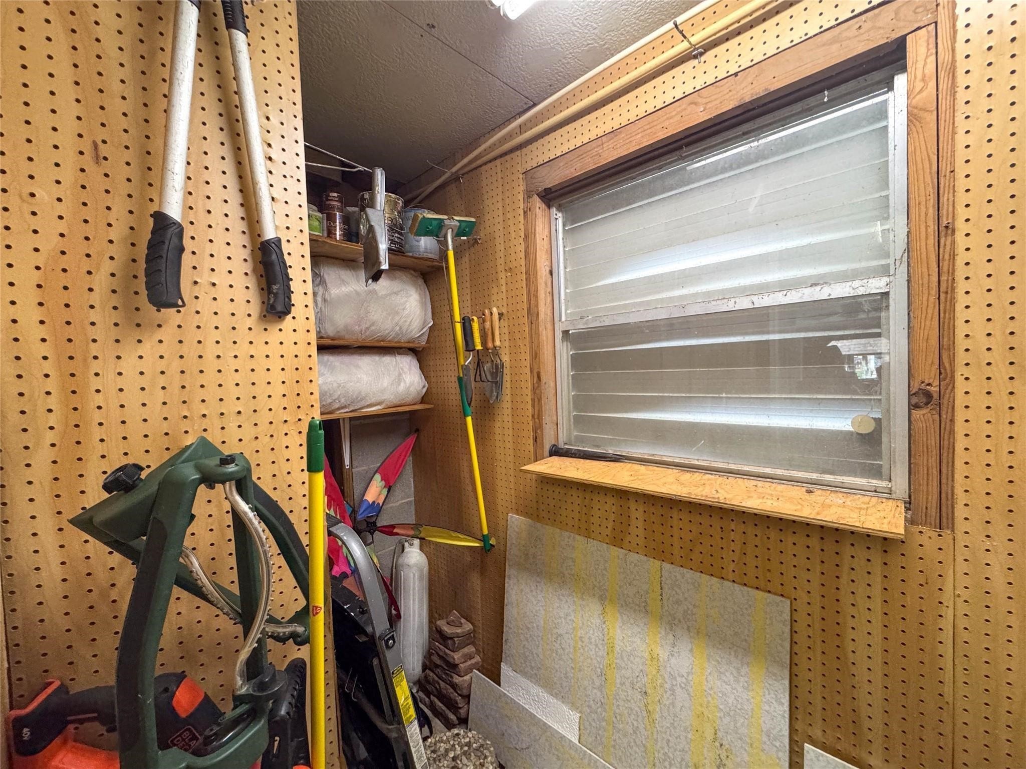This photo shows a compact storage space with pegboard walls, holding various tools and supplies. A small window provides some natural light, and shelves offer additional storage. Ideal for organizing garden or household tools.