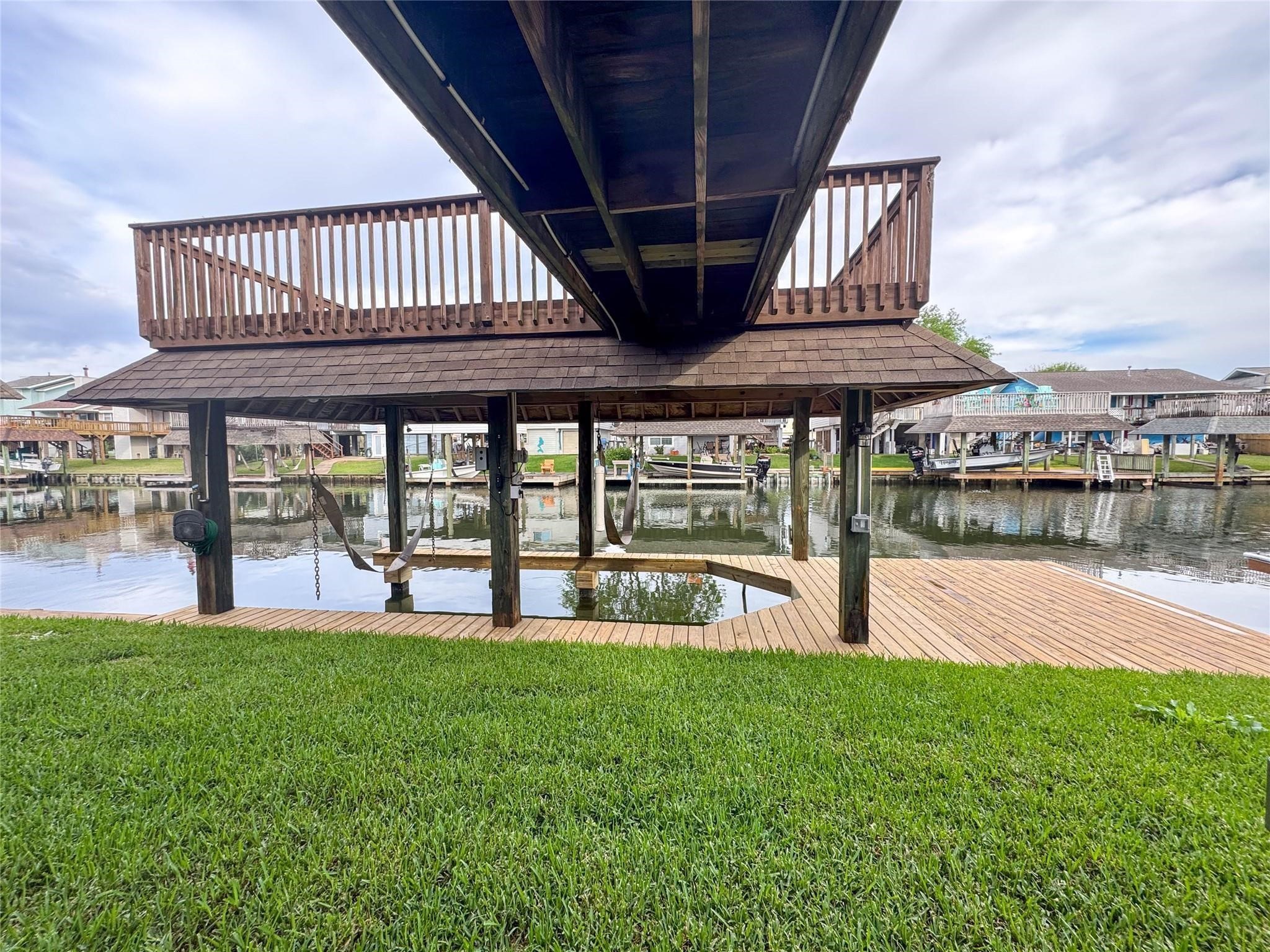 This photo showcases a waterfront property featuring a wooden dock with a covered boat lift and an upper deck. The area offers direct access to the water, perfect for boating enthusiasts. The surrounding neighborhood is visible across the canal, providing a serene, picturesque view.
