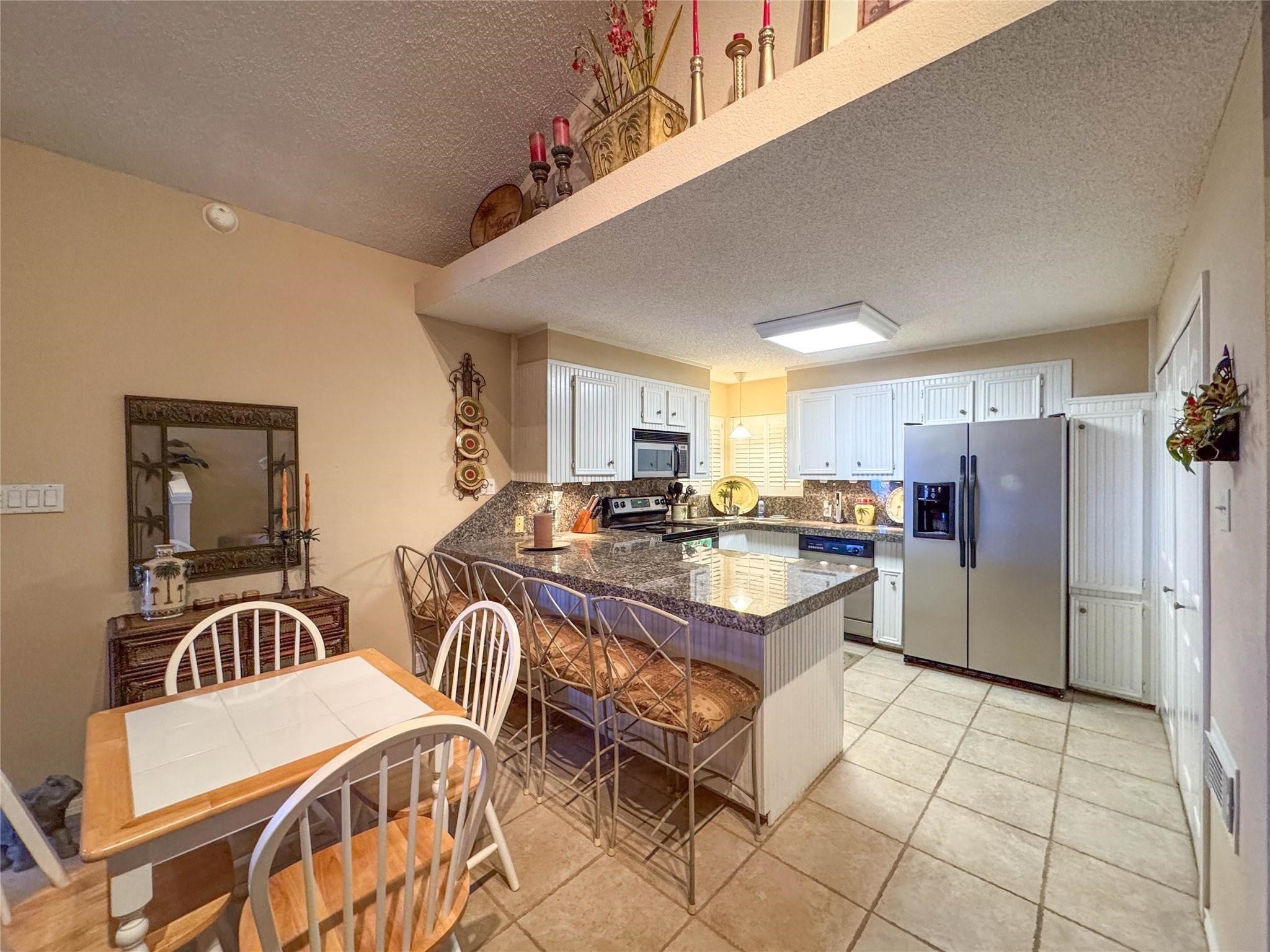This kitchen features a spacious layout with a central island, granite countertops, and stainless steel appliances. It offers ample cabinet storage, a cozy dining area, and decorative accents for a welcoming atmosphere.