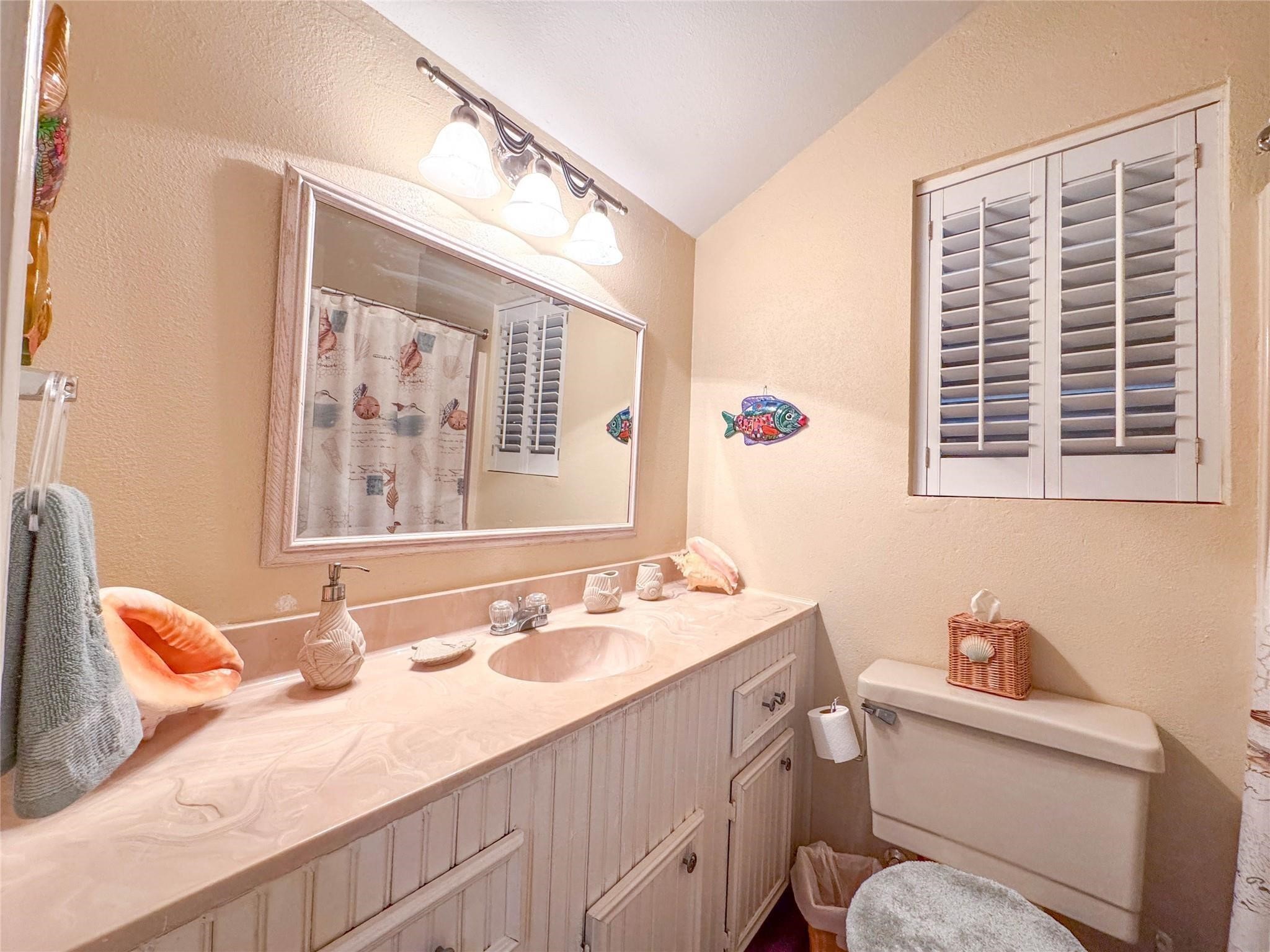 This cozy bathroom features a large vanity with ample storage, a decorative mirror, and a soft color palette. It includes a stylish light fixture, charming window shutters, and a whimsical fish decoration, creating a welcoming atmosphere.
