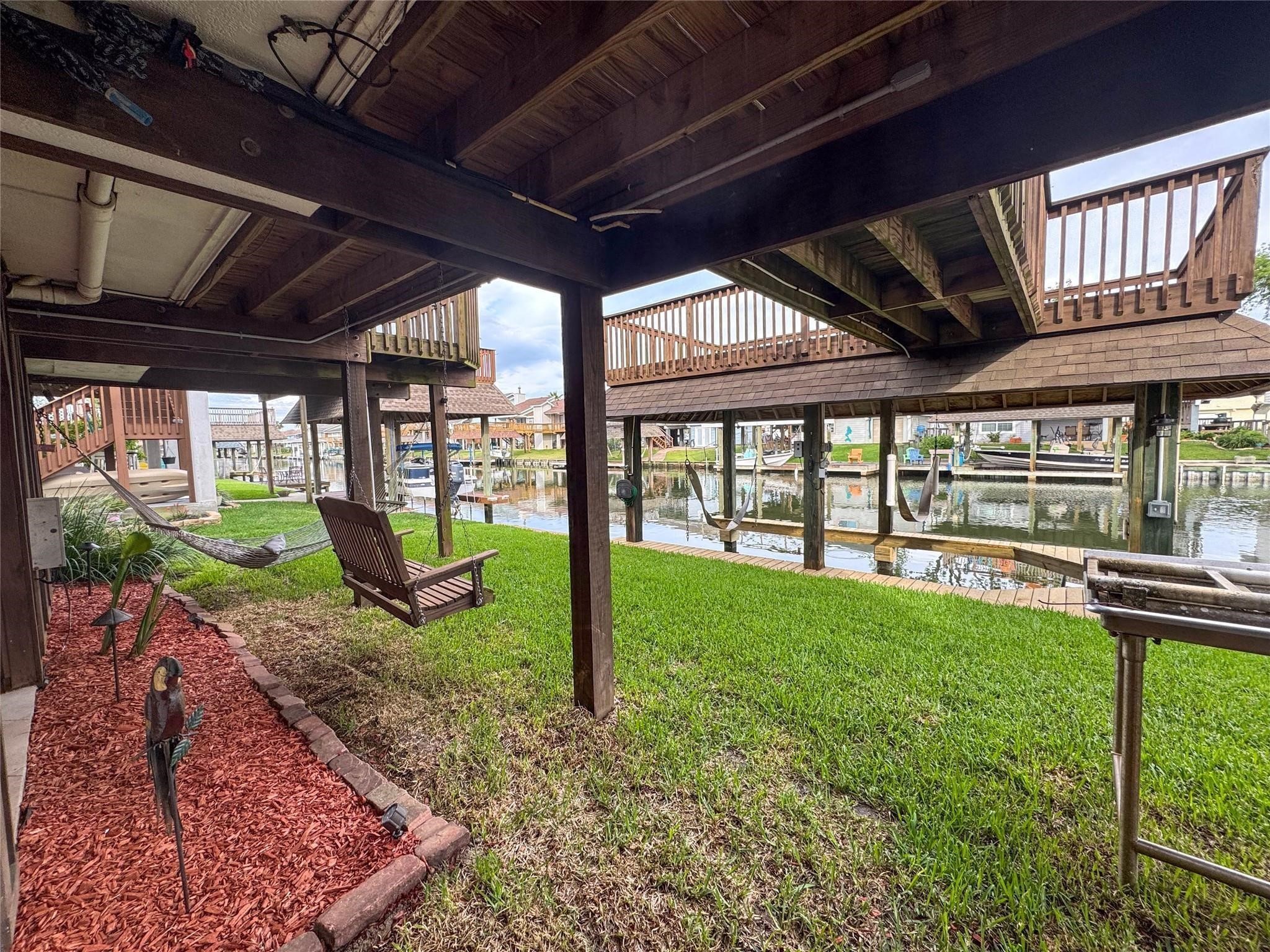 This photo showcases a serene waterfront area with a covered patio, lush grass, and a hammock. Ideal for relaxation and enjoying canal views, it offers a peaceful outdoor retreat.