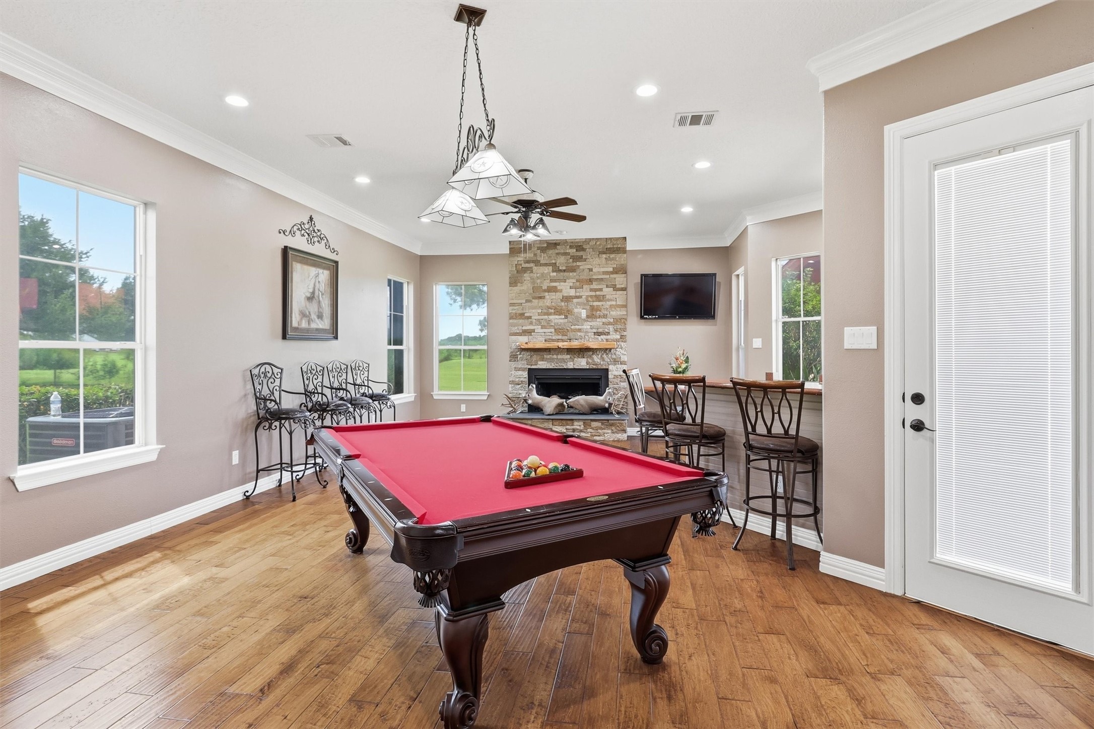 Entertainment awaits in this game room, complete with a stacked-stone fireplace, wall-mounted TV, and a built-in bar area with seating. Large windows bring in plenty of natural light, and a private door offers convenient outdoor access.
