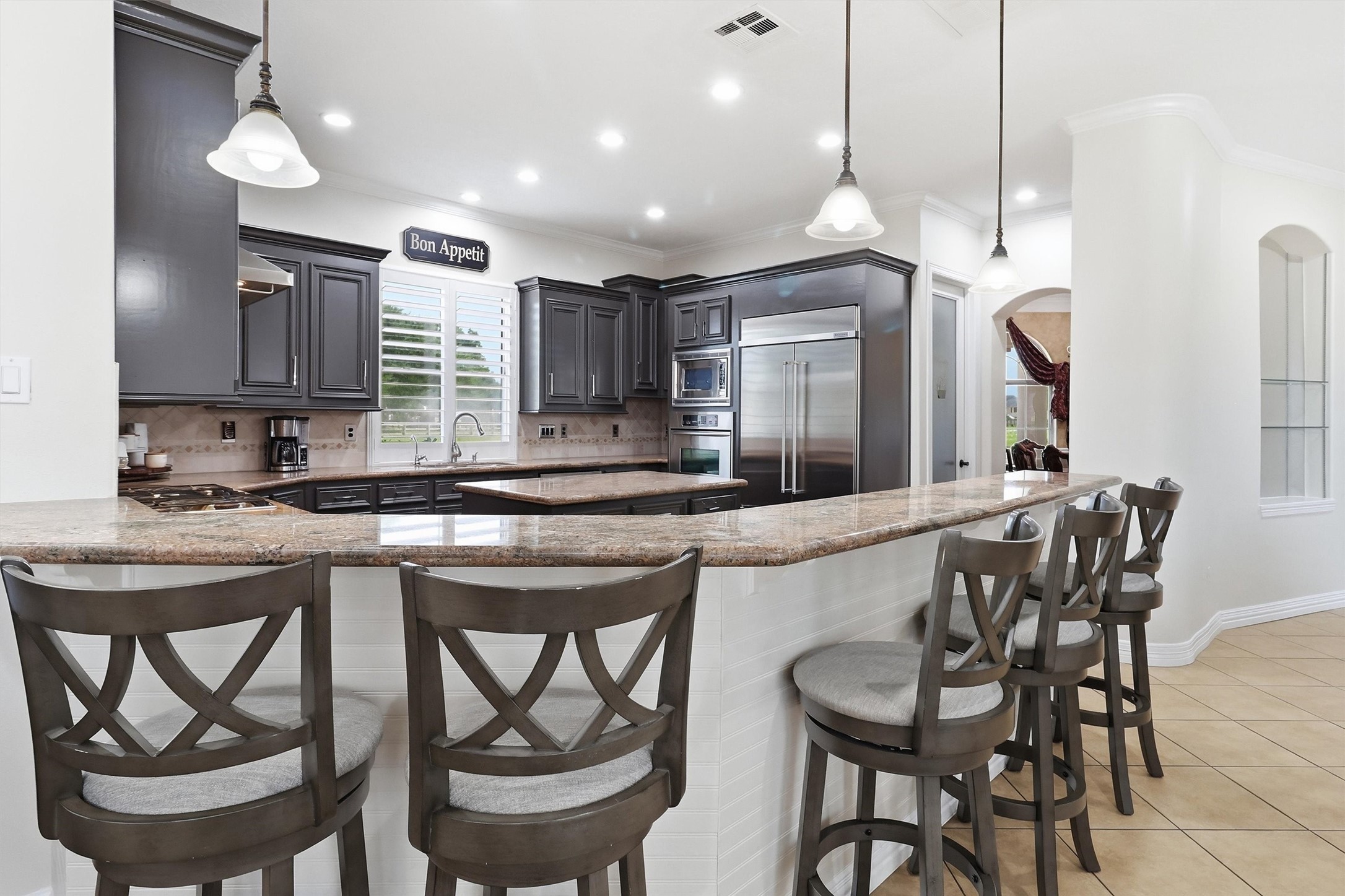 An oversized granite breakfast bar offers seating for the whole family, with a view into the fully equipped kitchen featuring stainless appliances and abundant cabinet space. The "Bon Appetit" charm adds a fun finishing touch!