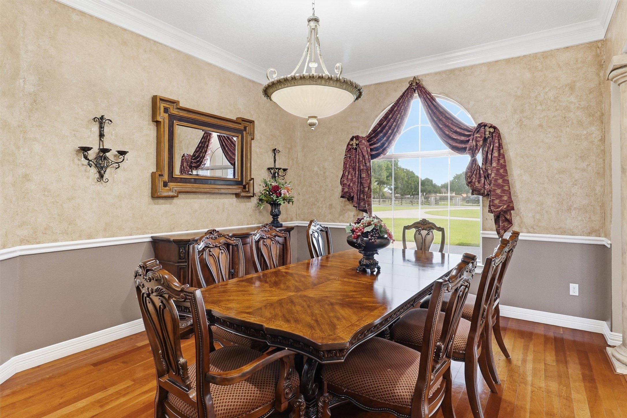 This elegant formal dining room features rich hardwood flooring, a decorative chandelier, and an arched window dressed with luxurious draperies. Ample space for a large dining table makes it perfect for hosting memorable gatherings.