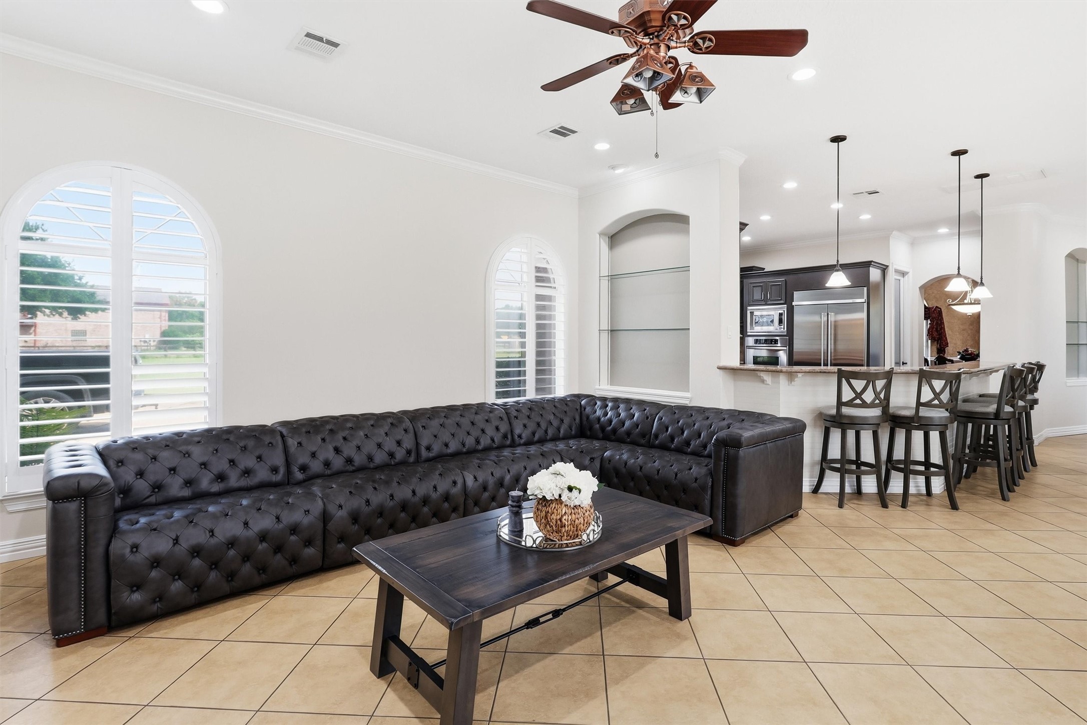 An expansive sectional anchors this comfortable living space, which flows seamlessly into the kitchen beyond. Arched windows with plantation shutters bring in natural light and add architectural charm.