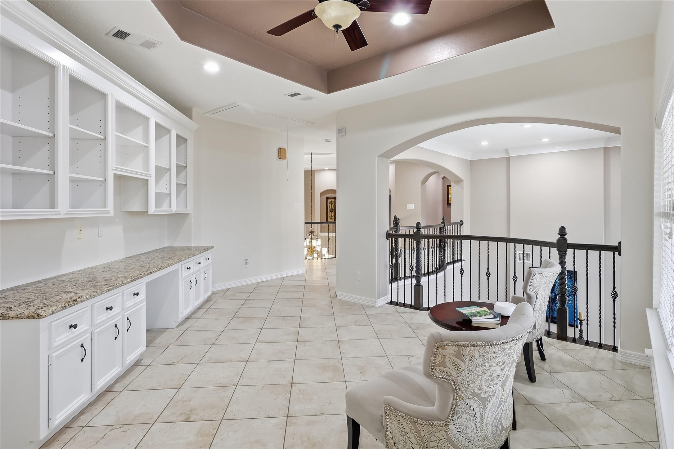 This versatile upstairs landing offers built-in cabinetry and granite countertop space, perfect for a home office or hobby nook. A wrought iron railing overlooks the entry below, adding architectural interest.