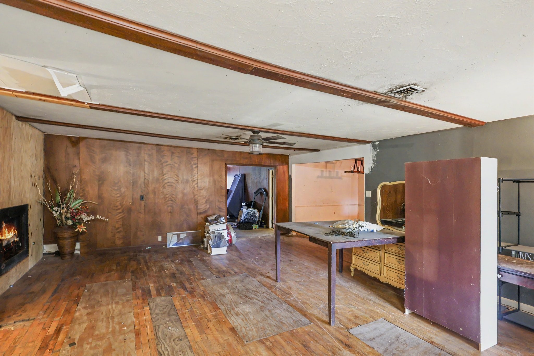 Living area featuring a fireplace, wood paneling and ceiling beams. Renovations needed.