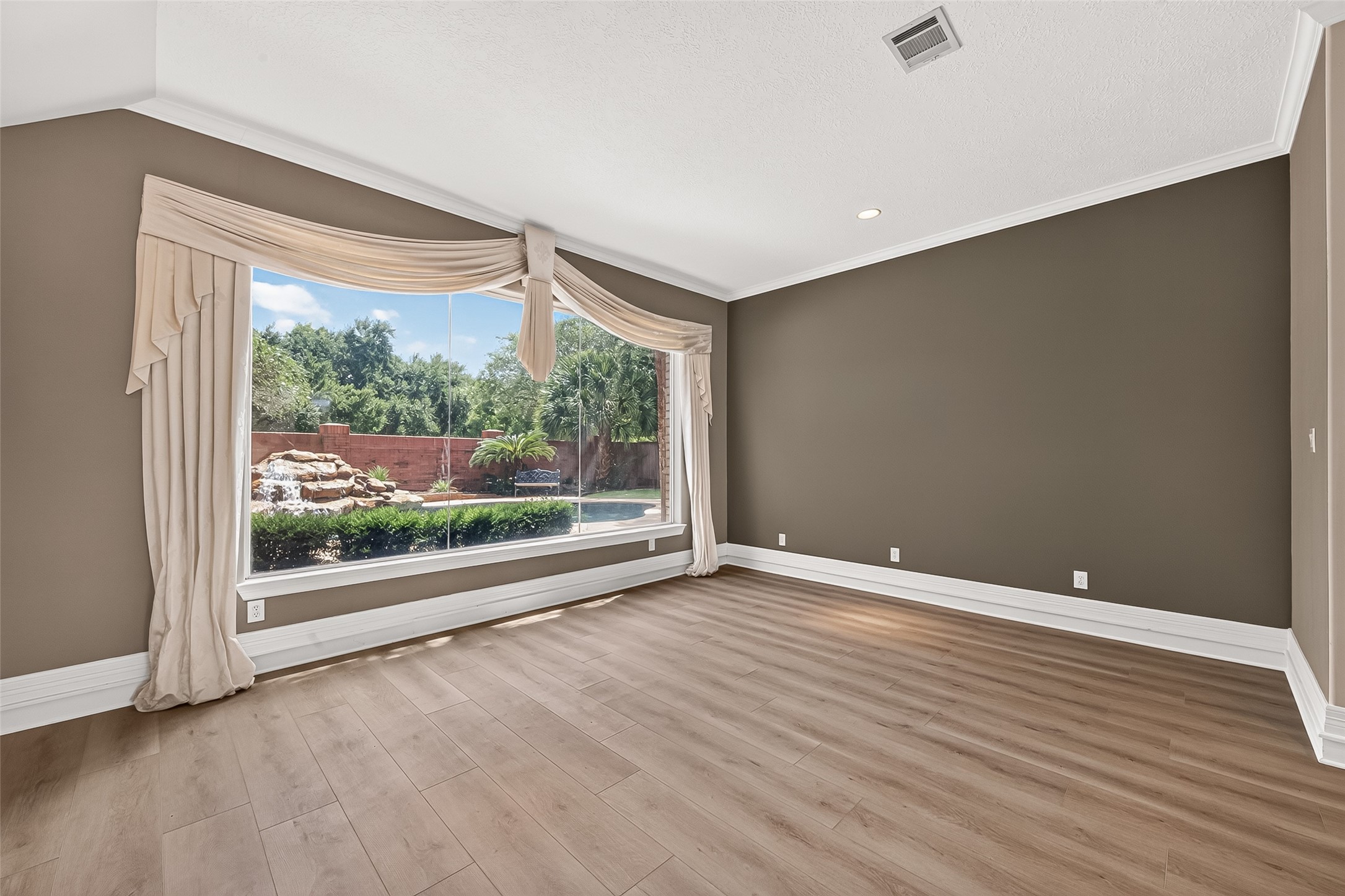 Formal sitting room with beautiful LVP flooring and huge large windows offering a stunning view of the pool/spa and waterfall feature