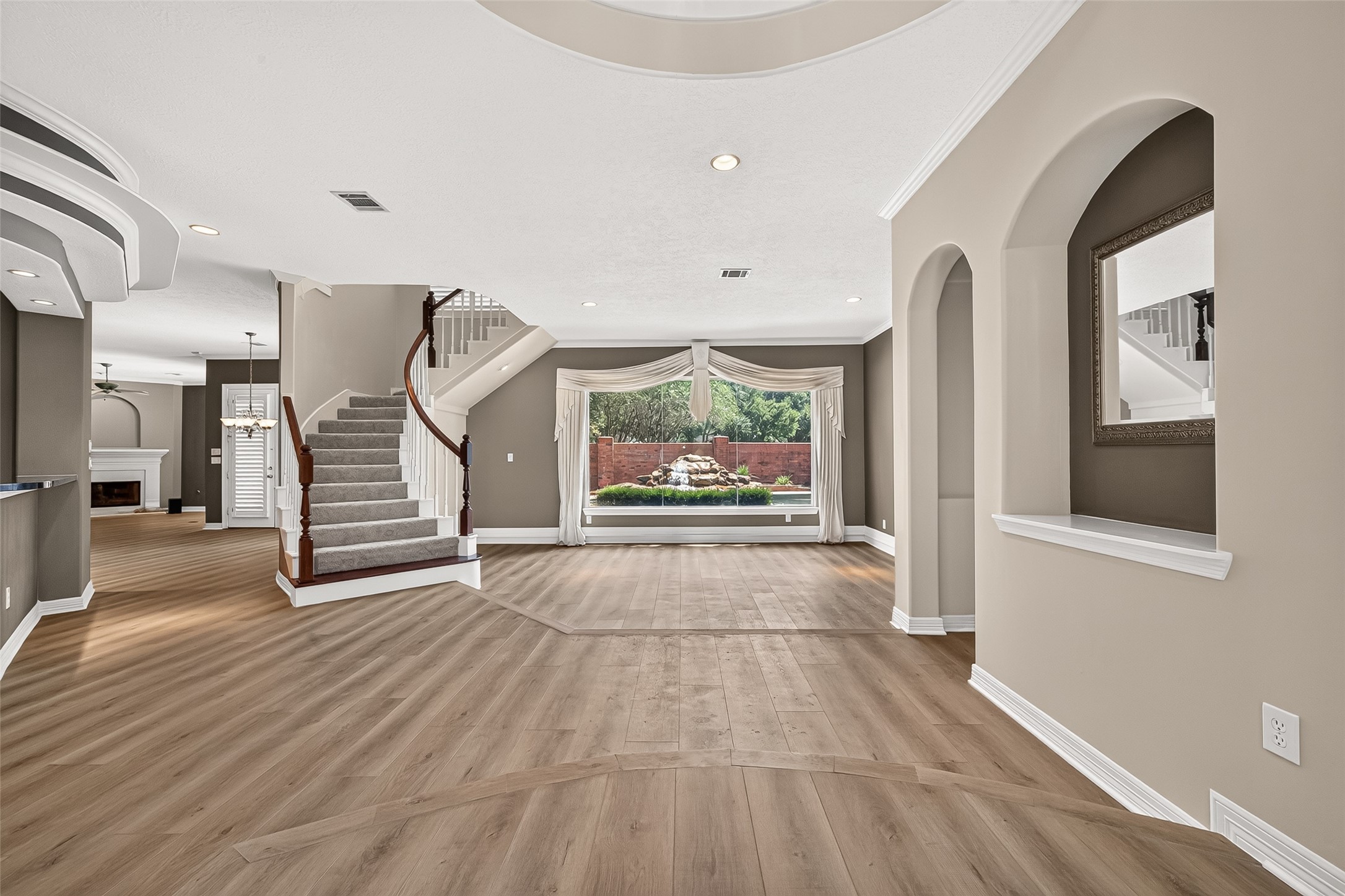 Amazing open-concept floor plan featuring a grand staircase, stylish arched openings, and a large window offering a stunning view of the backyard oasis