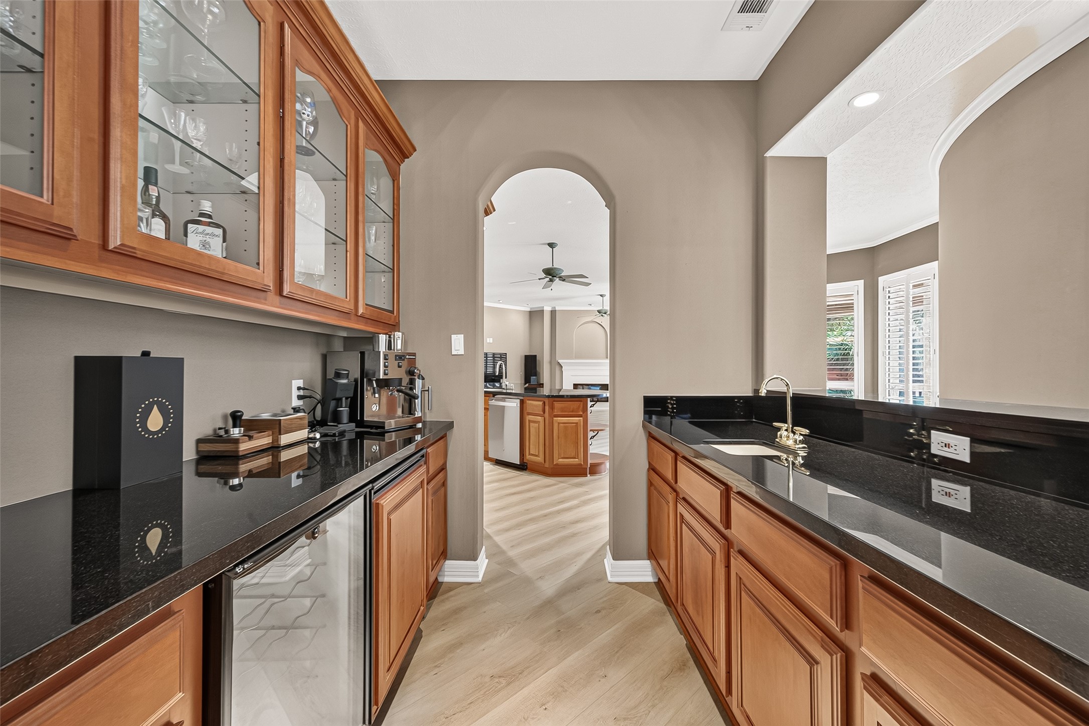 Amazing wet bar with rich wood cabinetry, sleek black countertops, and glass display cabinets, perfect for entertaining and enhancing your living space. Located right off the formal dining, kitchen, and sitting area, this space is perfect for entertaining!