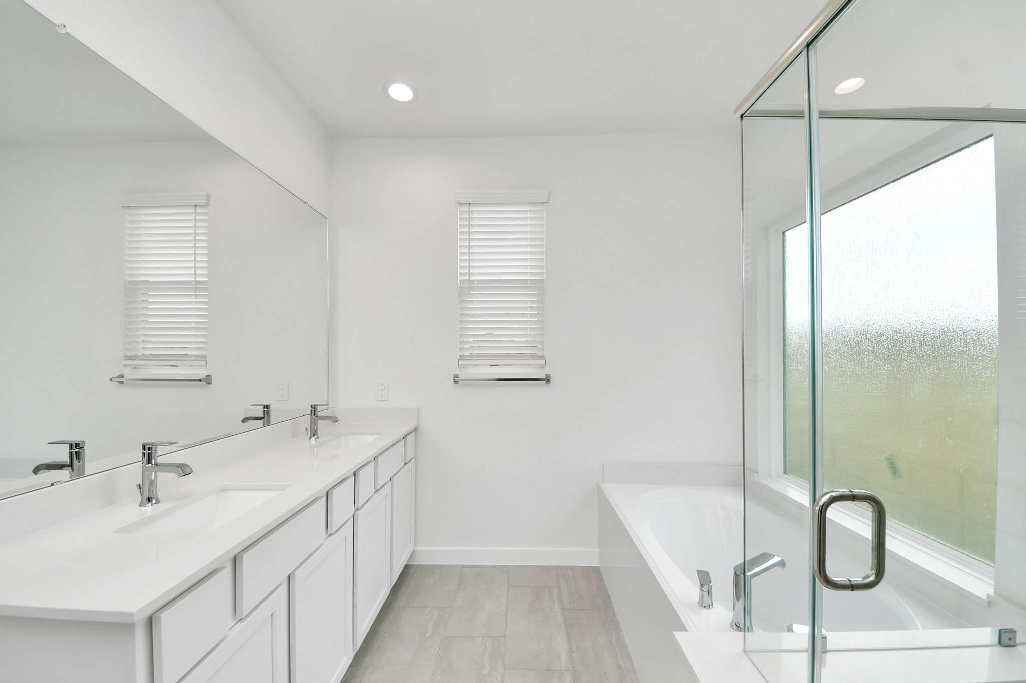 Escape to a spa-like oasis in this primary bathroom. Enjoy a walk-in shower with tile surround, a separate garden tub with custom detailing, and an elegant vanity featuring light countertops, modern hardware, and beautiful vanity lights. Experience luxury and relaxation in every detail. Sample photo of completed home with similar floor plan. Actual colors and selections may vary.