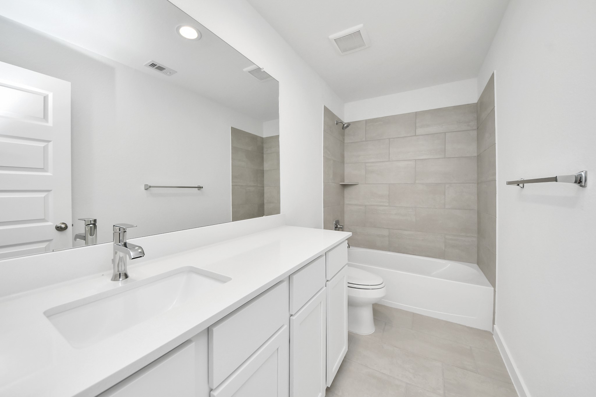 Secondary bath features tile flooring, bath/shower combo with tile surround, light stained wood cabinets, beautiful light countertop. Sample photo of completed home with similar floor plan. Actual colors and selections may vary.