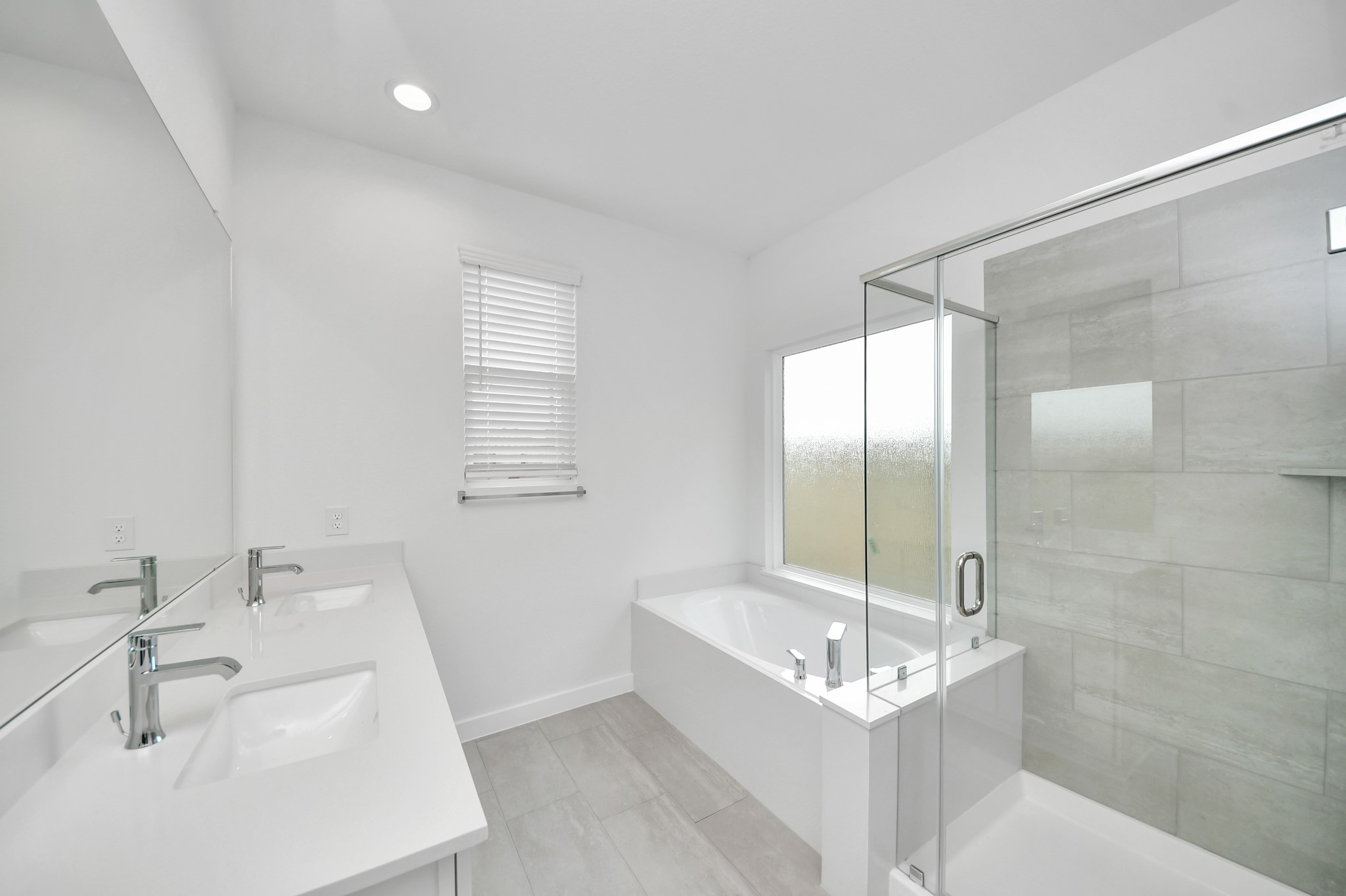 Indulge in a spa-like retreat within the confines of this primary bathroom. Delight in a spacious walk-in shower enveloped in stylish tile surround, unwind in a separate garden tub adorned with custom detailing. Sample photo of completed home with similar floor plan. Actual colors and selections may vary.