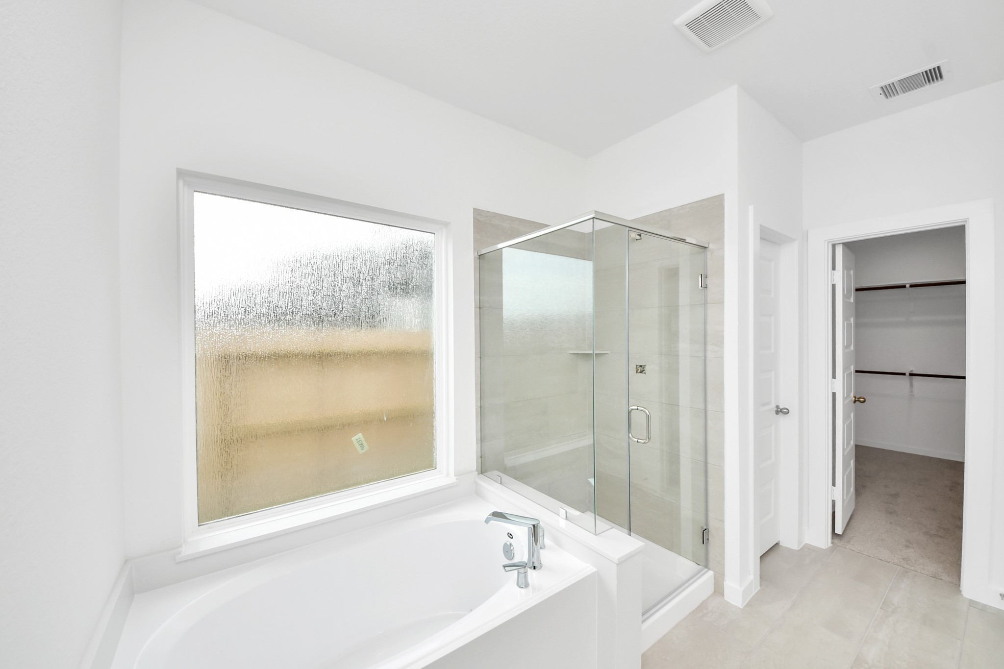 Indulge in a spa-like retreat within the confines of this primary bathroom. Delight in a spacious walk-in shower enveloped in stylish tile surround, unwind in a separate garden tub adorned with custom detailing. Sample photo of completed home with similar floor plan. Actual colors and selections may vary.
