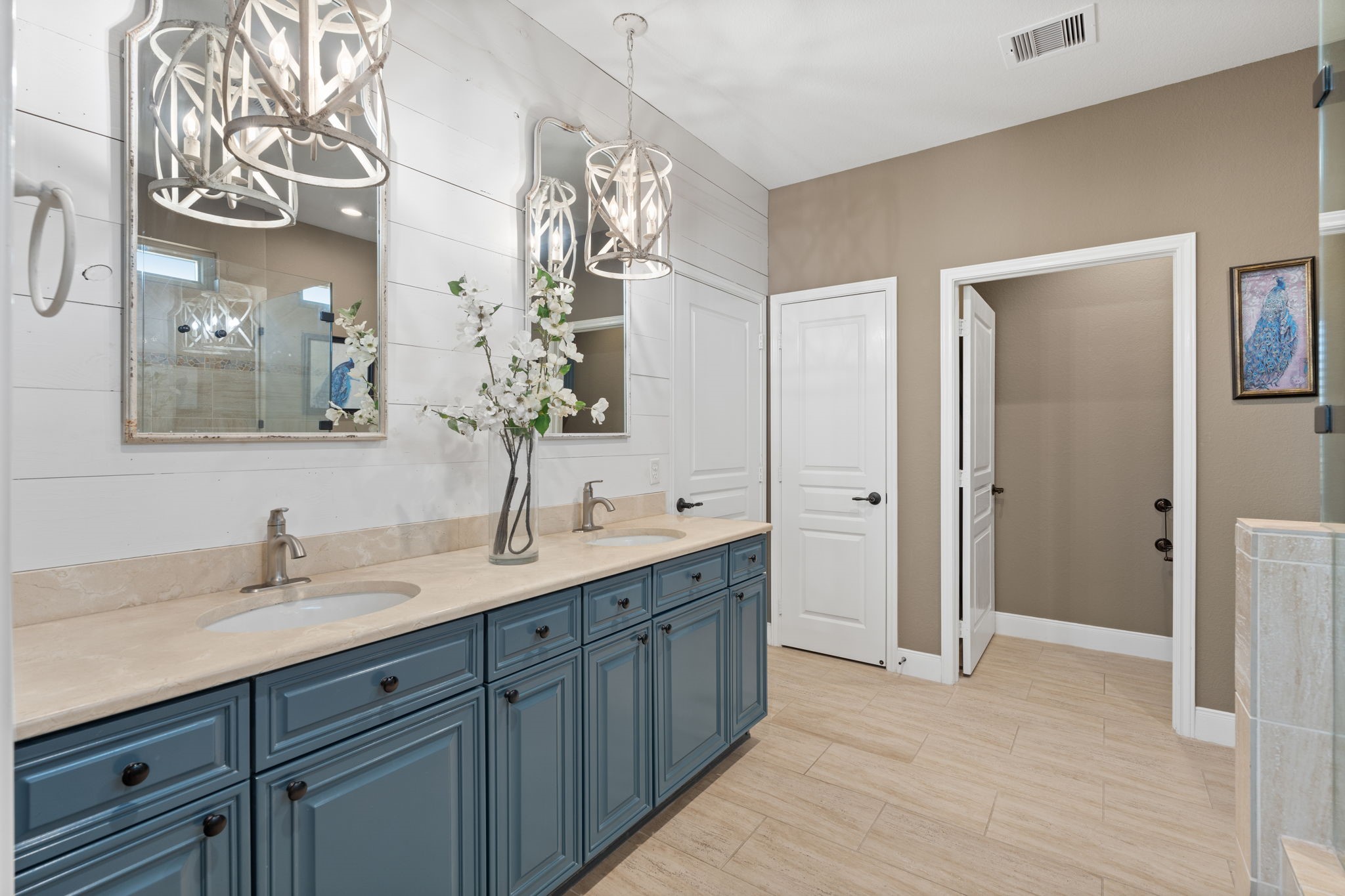Elegant white pendants with candelabra bulbs gracefully dangle in front of the dual vanities, casting a warm glow over the framed mirrors. A perfect touch that ties together Modern Farmhouse dcor with timeless charm.