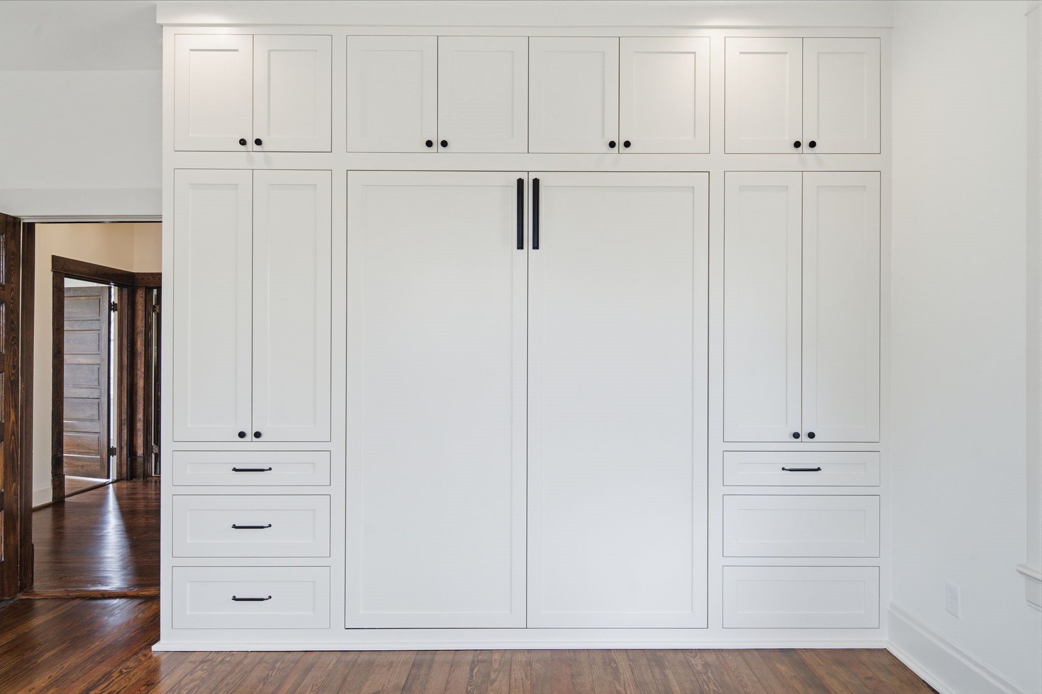 Built-in Murphy bed and cabinetry offers ample storage with sleek white finishes and contrasting black hardware.