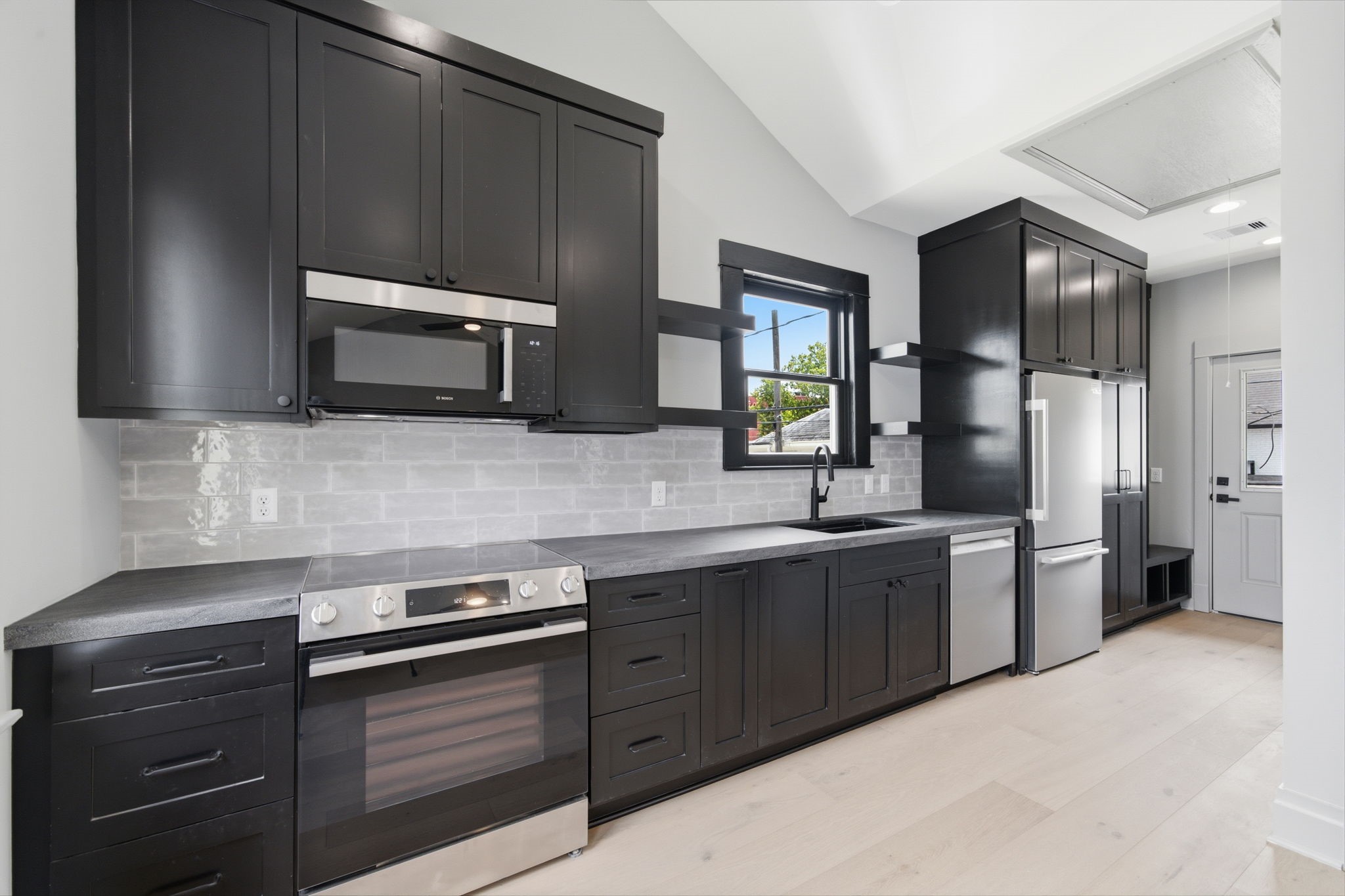 The APARTMENT: Custom kitchen featuring classic black cabinetry, stainless steel appliances complemented by ample natural light.