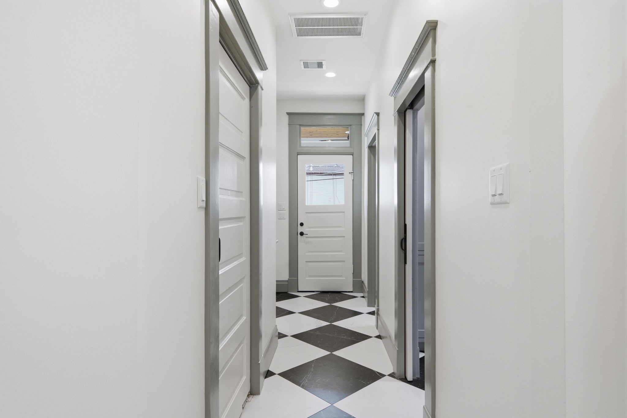 Leading to the back of the home, the hallway with elegant checkered tile flooring. the main house features all the original doors, including the one leading to a back yard.