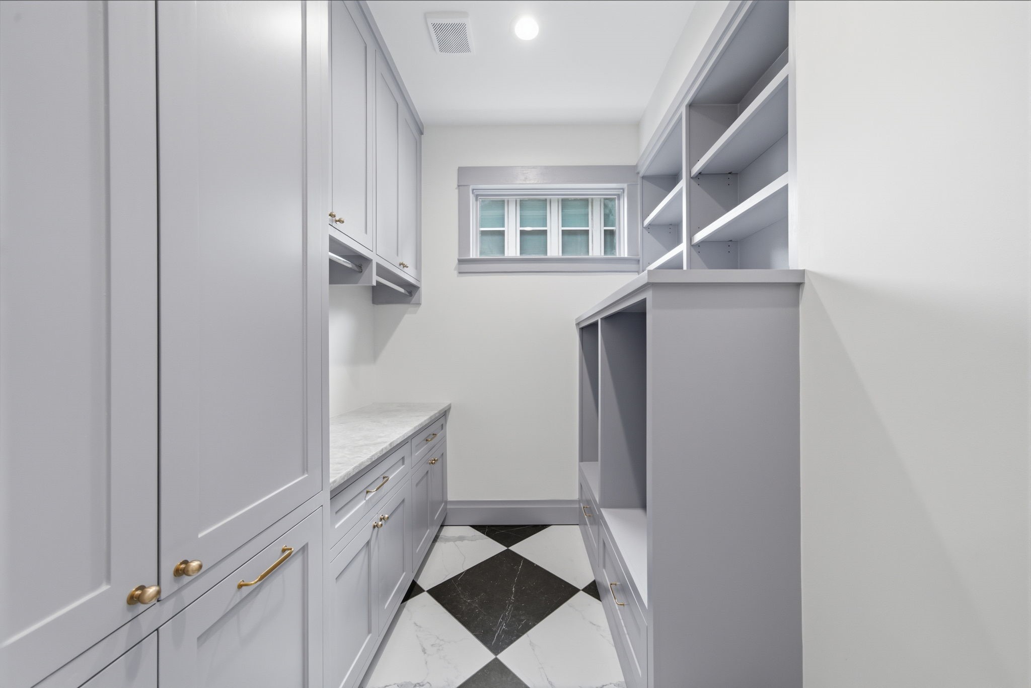 Spacious laundry room with built in risers, ample storage, featuring custom cabinetry, quartz countertop and space for folding and hanging.