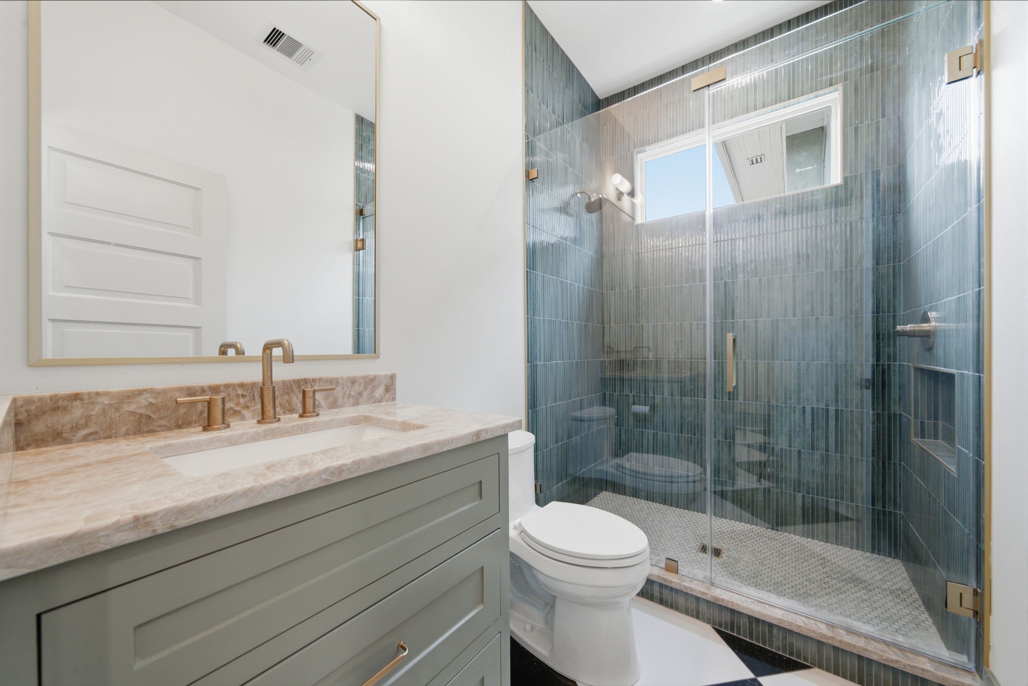 Downstairs full bathroom featuring a glass-enclosed shower, stylish vanity with a quartz countertop, and sleek Delta brushed gold fixtures.