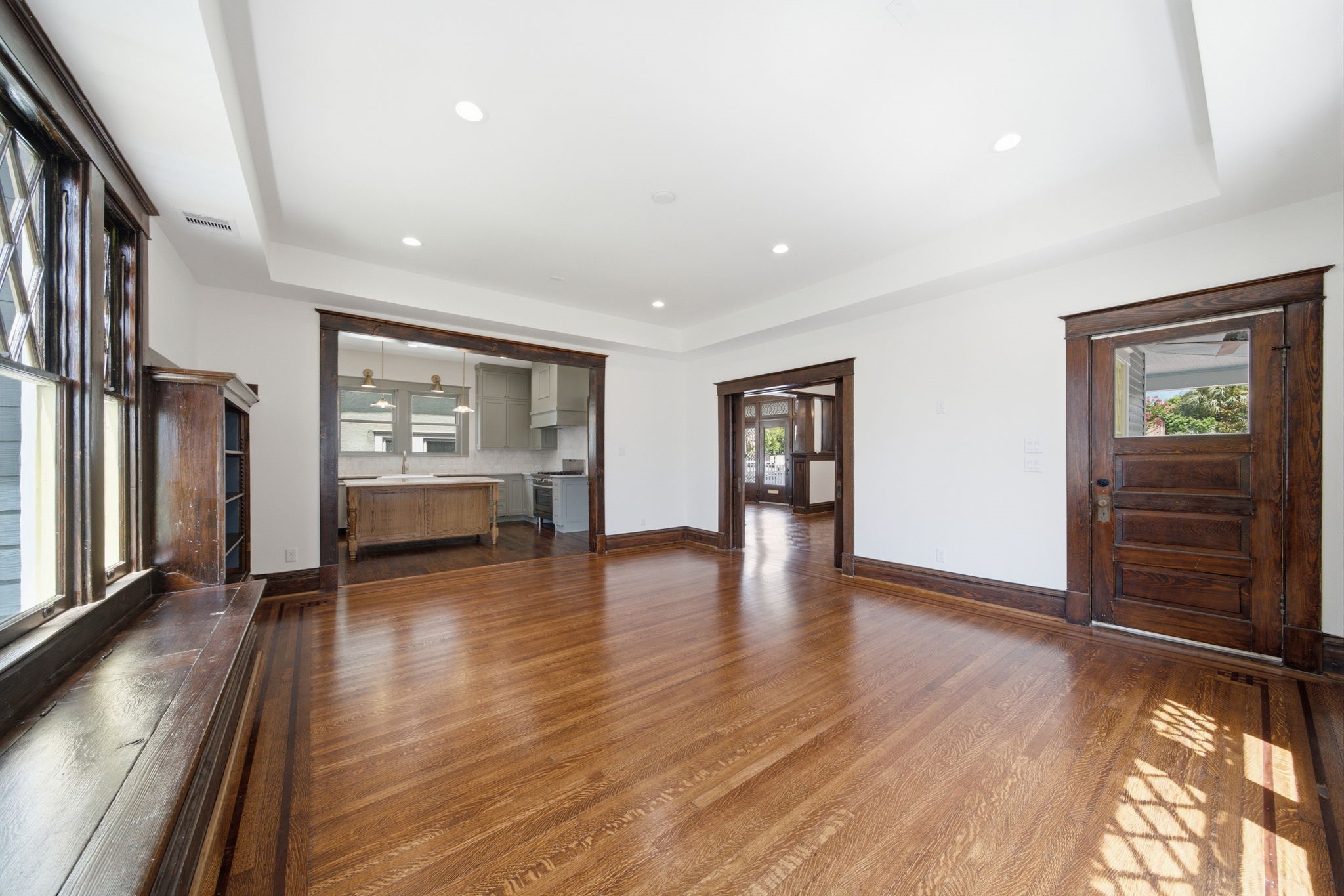The large living room area continues to highlight the hardwood floors, elegant wood trim, and abundant natural light, seamlessly connecting to a modern kitchen and dining areas. It also connects to the wrap around porch.