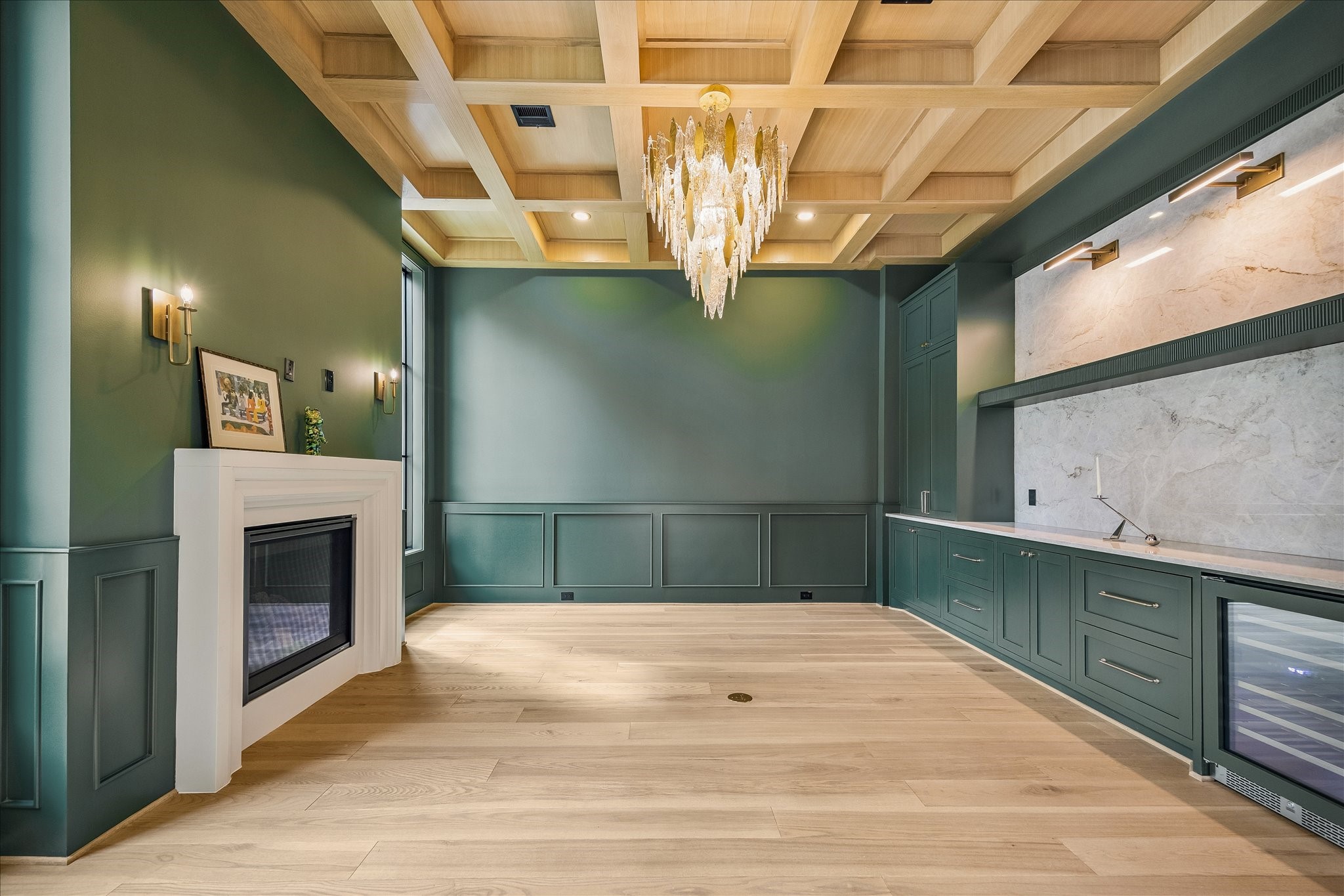 The elegant coffered ceiling adds a touch of sophistication to the room, while the inviting gas fireplace, accented with warm wood details, creates a cozy atmosphere. The built-in bar area provides convenient storage space for beverages.