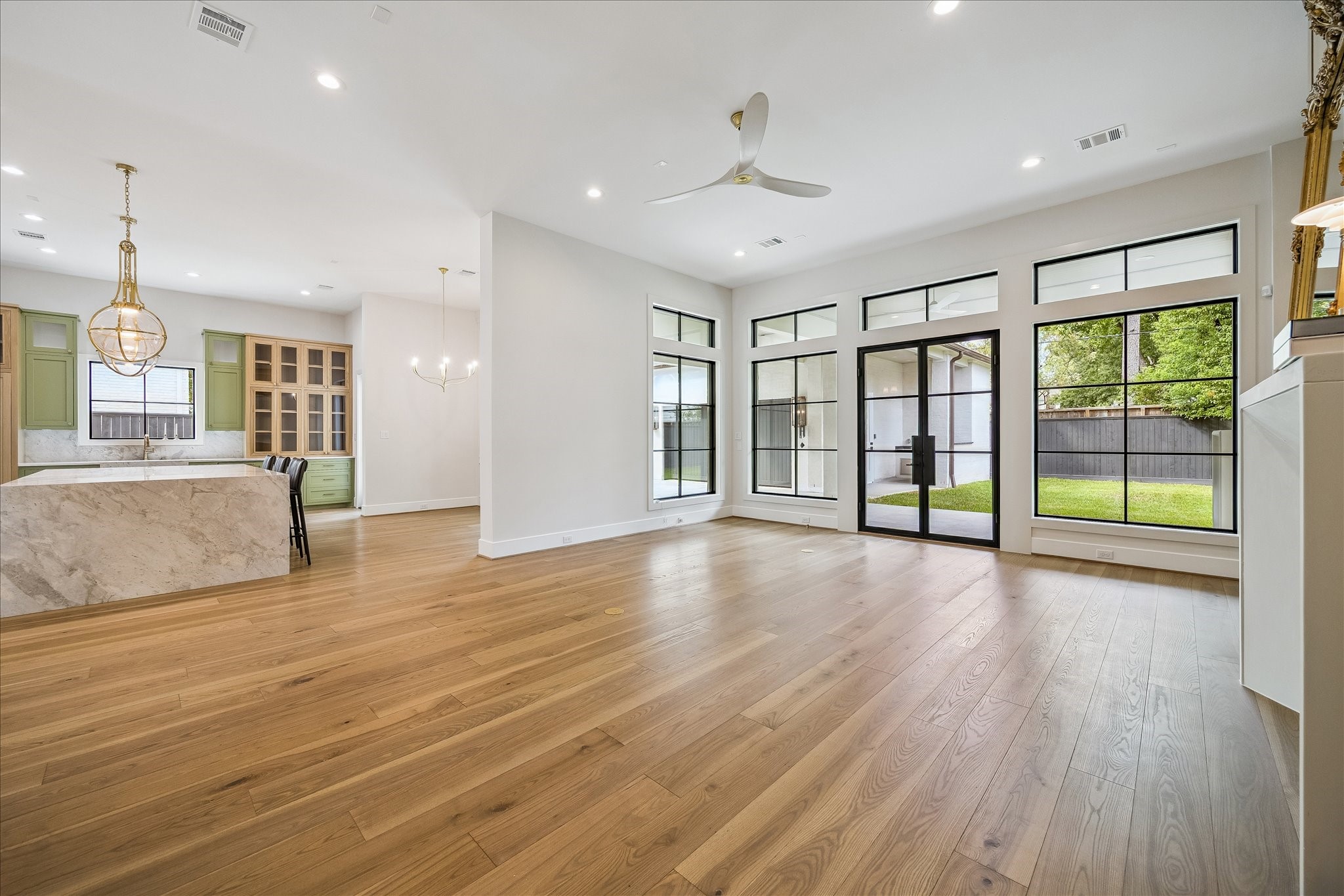 The living room is a bright and welcoming space, featuring floor-to-ceiling windows that provide stunning views of the backyard. A gas fireplace with a white oak surround adds warmth and elegance to the room. Steel-framed doors open to a covered patio, seamlessly connecting the indoor and outdoor living areas, enhancing the versatility and enjoyment of the space.