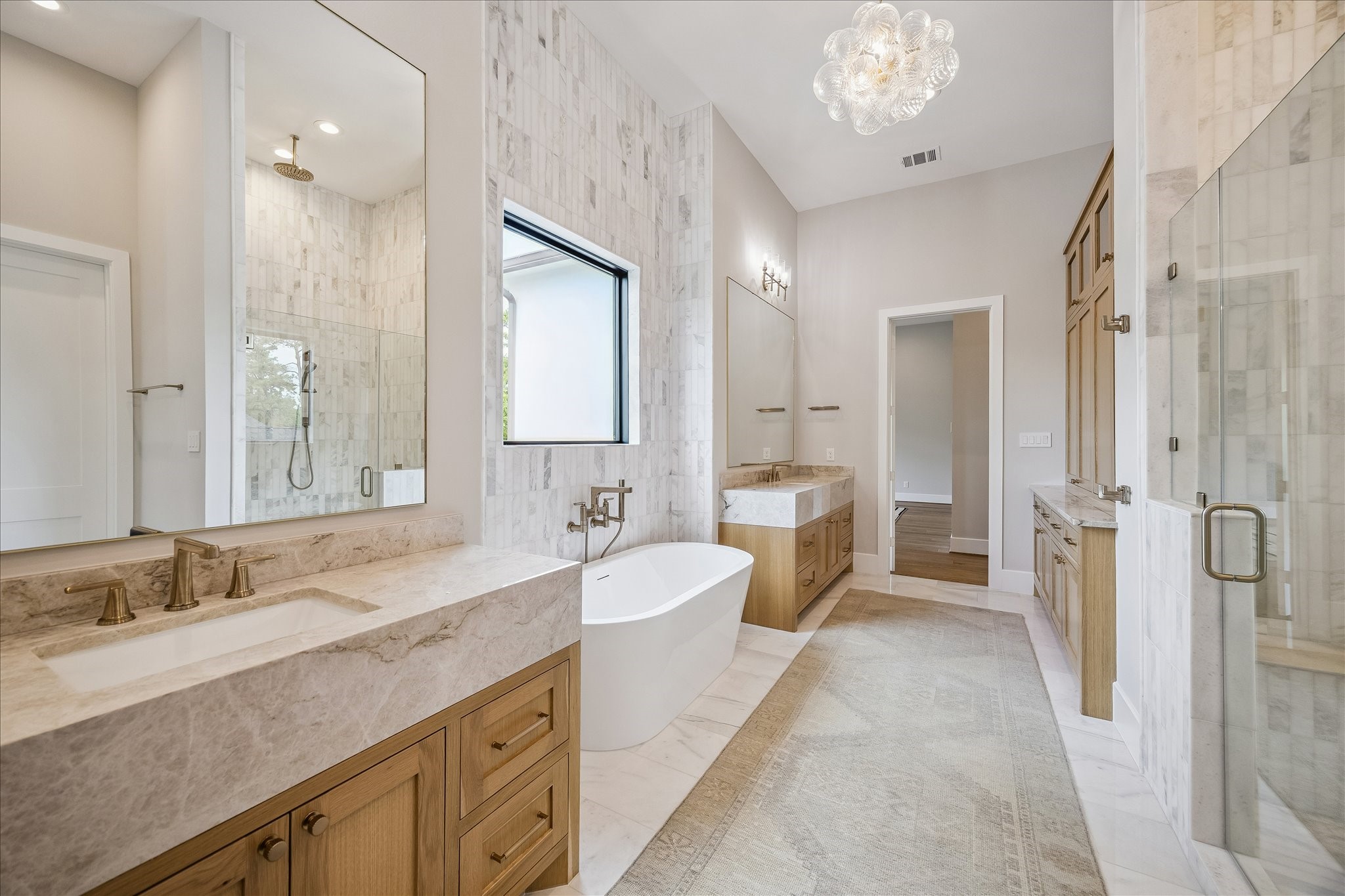 The primary retreat boasts ceilings that create an expansive and airy feel. The bathroom is beautifully appointed with Taj Mahal quartzite separate vanities, a freestanding acrylic soaking tub, and an oversized glass-enclosed shower featuring dual fixtures.