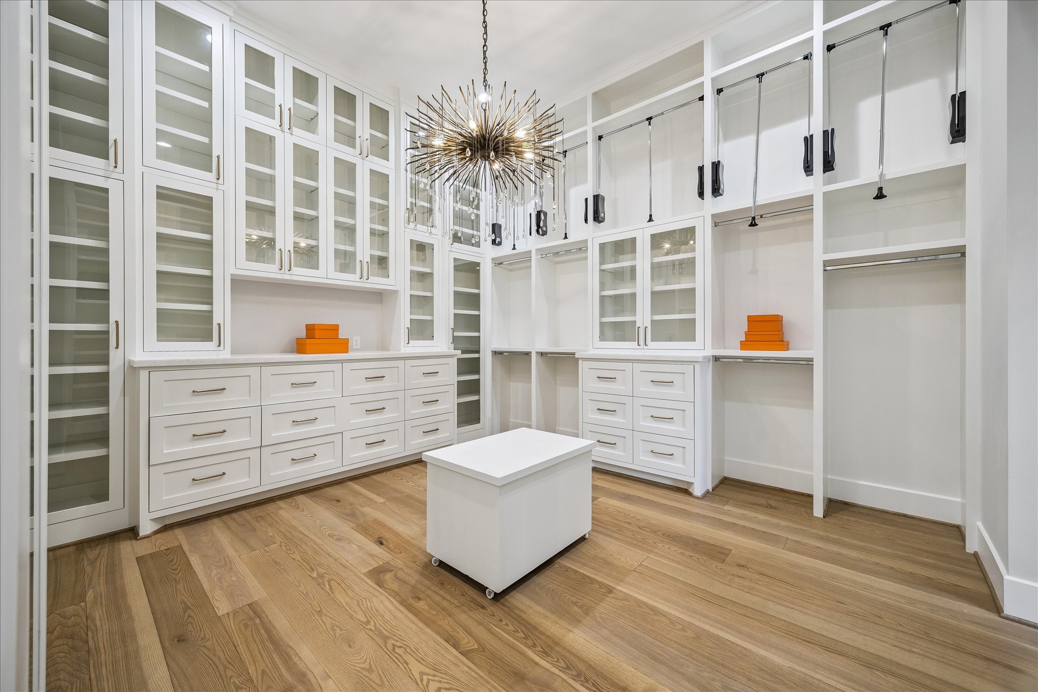 The custom wardrobe system is designed for maximum organization and includes glass-front cabinetry, built-in dresser towers, pull-down hanging racks, and abundant shelving and drawers.
