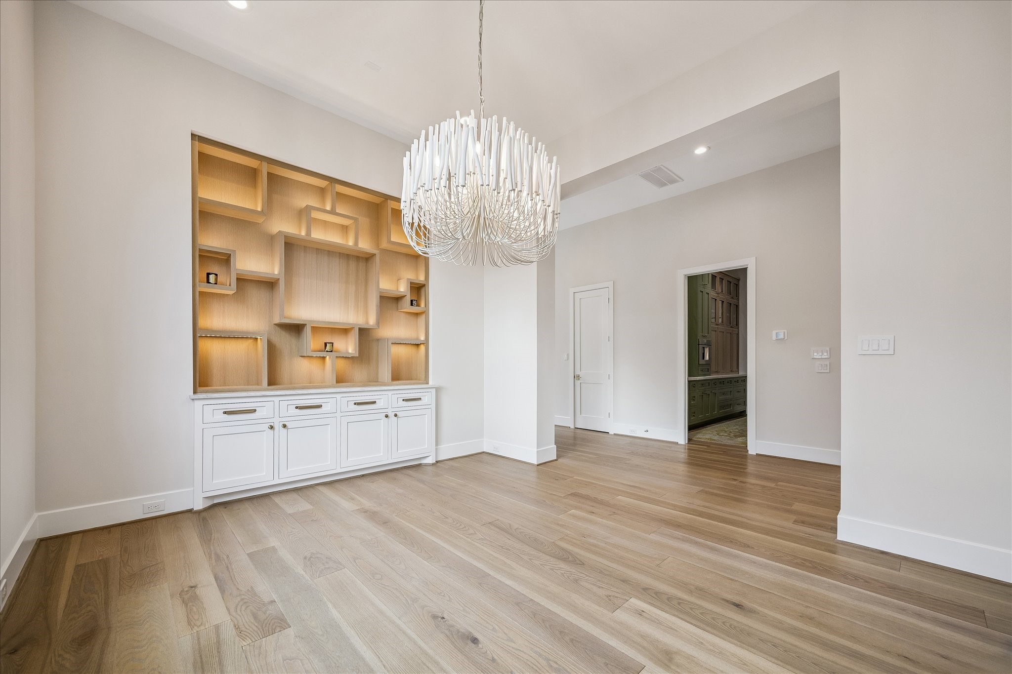 Forma Dining area features white oak cabinetry with integrated display shelving. Designer chandelier providing warm architectural presence.