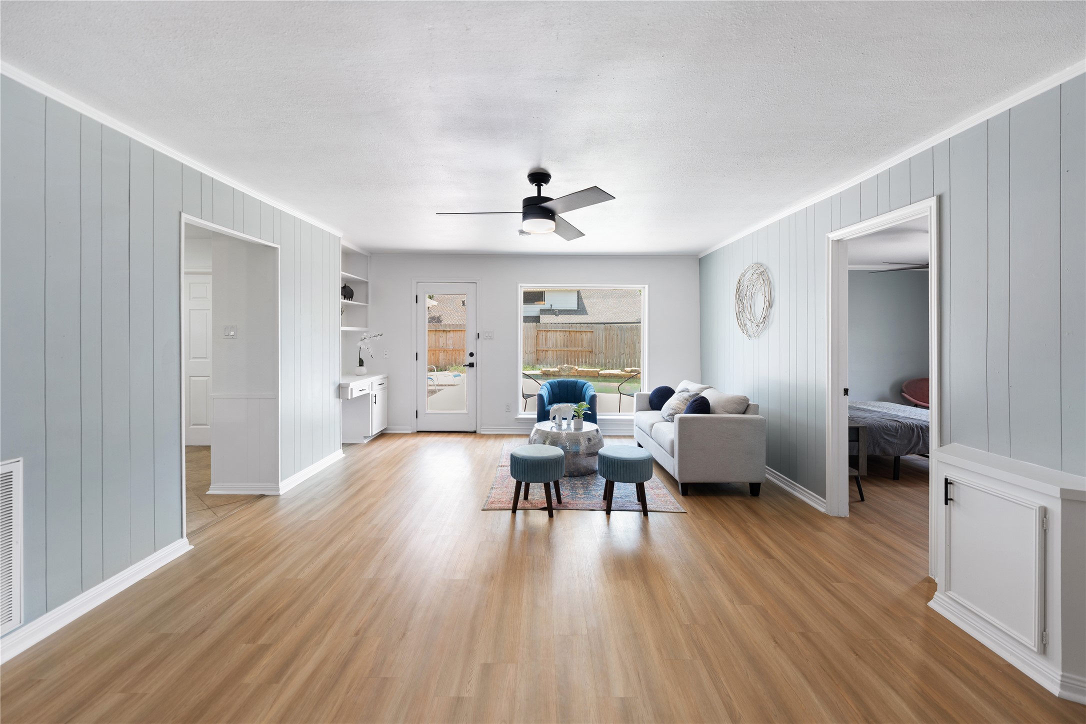 The luminous living room with wood flooring and a soft, modern palette, has a splendid view of the pool area.