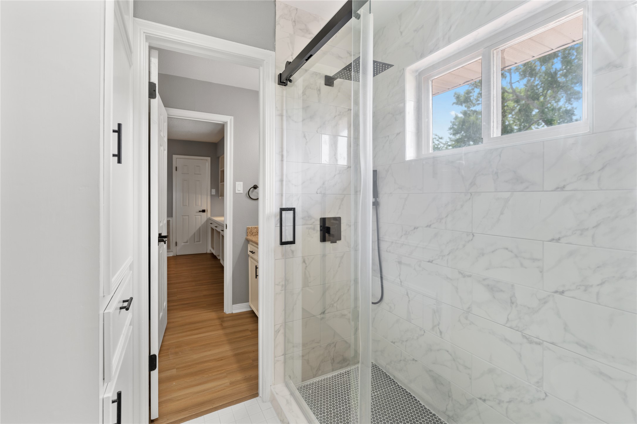 The secondary bathroom features a luxurious glass-enclosed shower with marble-style tiles and a rain showerhead.