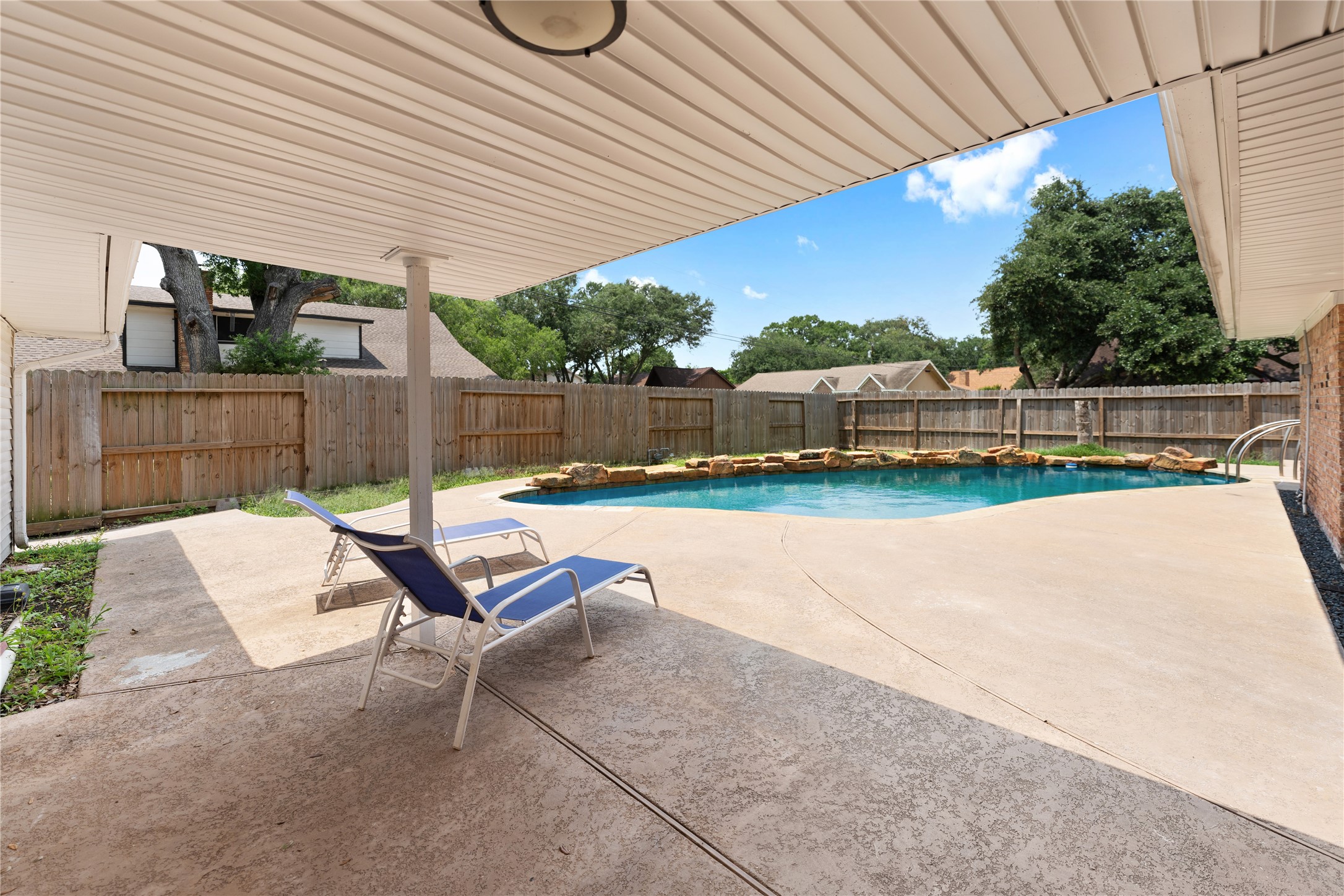 The backyard features an ample covered area surrounding the sparkling pool, ample enough to accommodate a table and lounging chairs