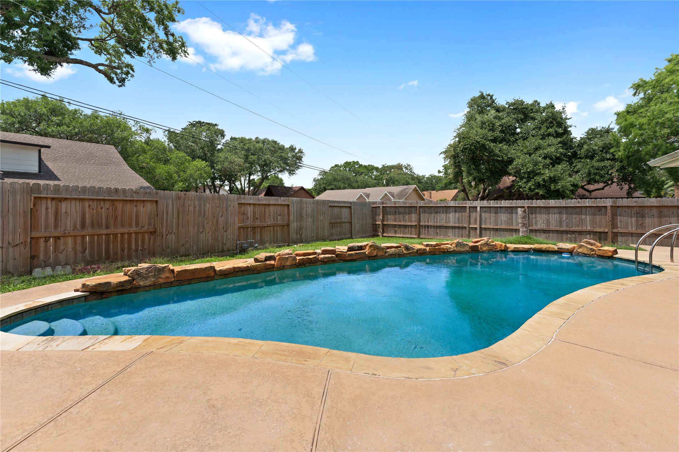 The in-ground swimming pool is bordered by natural stone accents and a spacious concrete patio, offering a relaxing outdoor space.