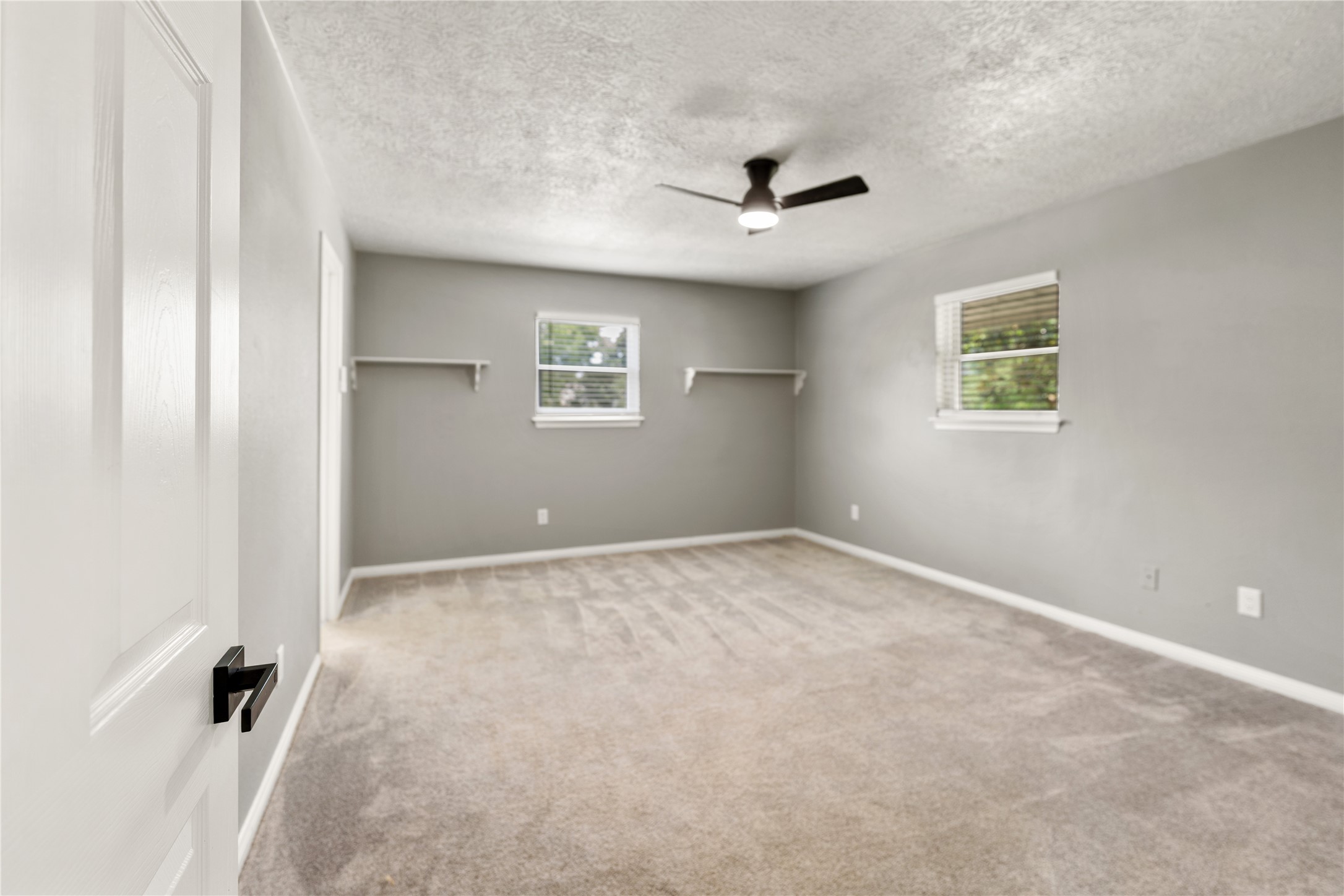 One of two spacious secondary bedrooms with carpeted flooring, featuring two windows that provide natural light. It has a modern ceiling fan and wall-mounted shelves, offering a versatile space for personalization.