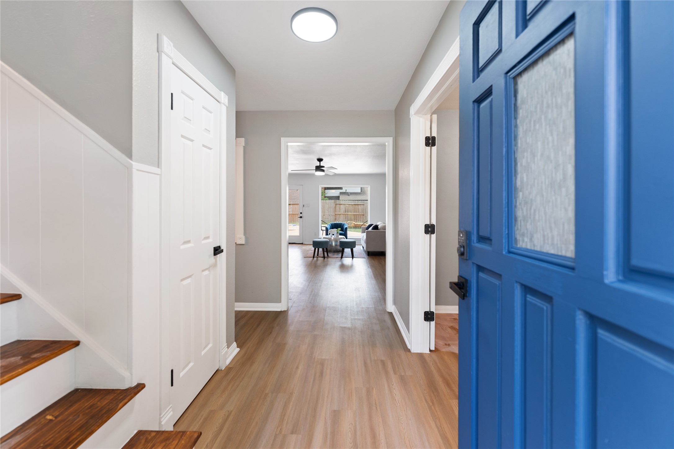 Welcome to the bright entryway, featuring a vibrant blue door, sleek wood flooring, and neutral walls leading to the inviting living area