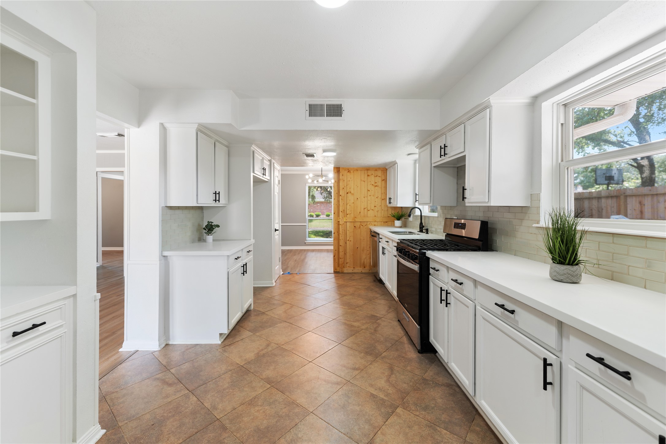 The kitchen features a modern, spacious design with white cabinetry and contrasting black hardware. It has ample counter space, gas stove, and large windows for natural light, creating an inviting cooking environment.